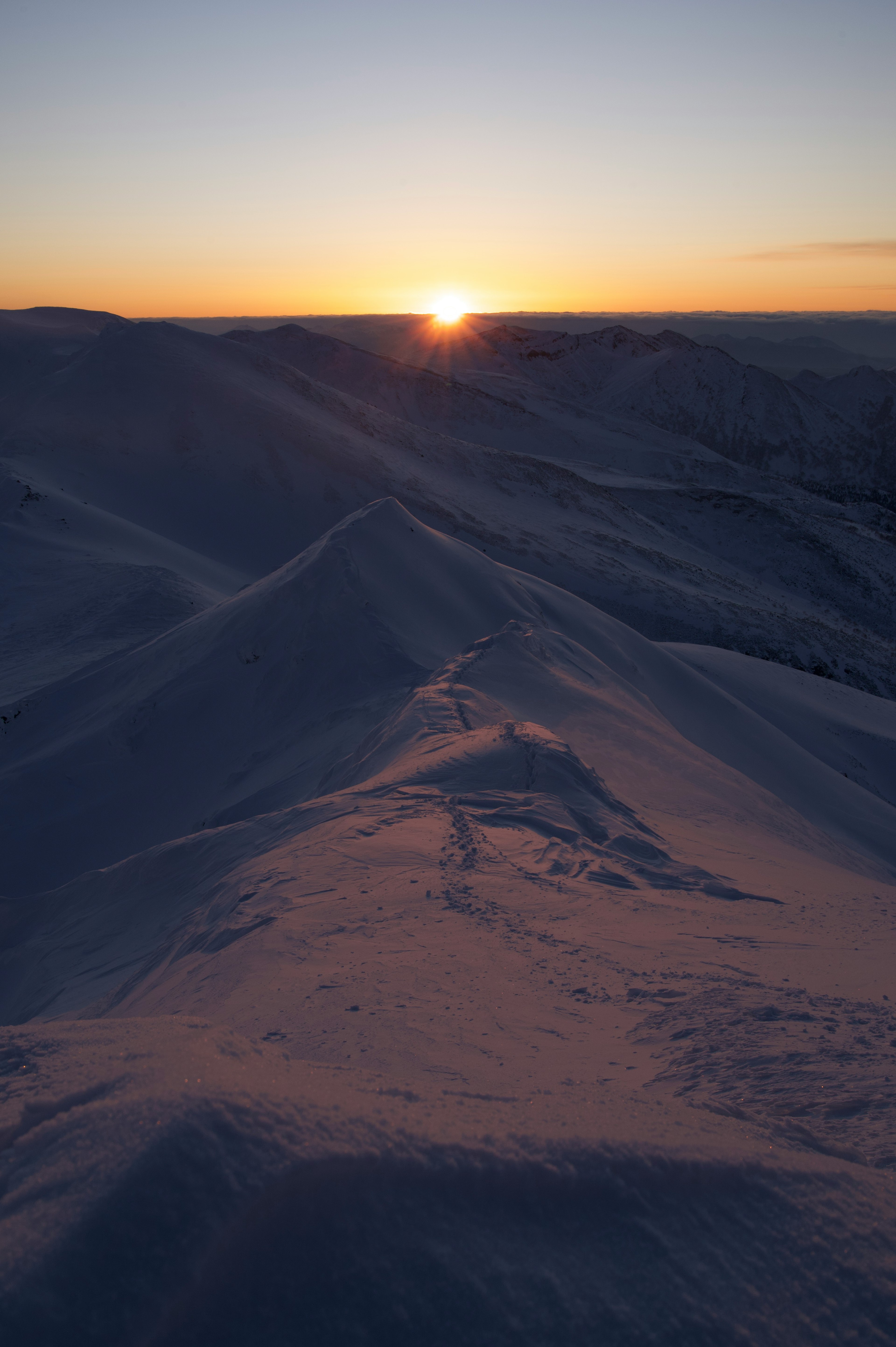 雪に覆われた山の稜線と夕日の風景