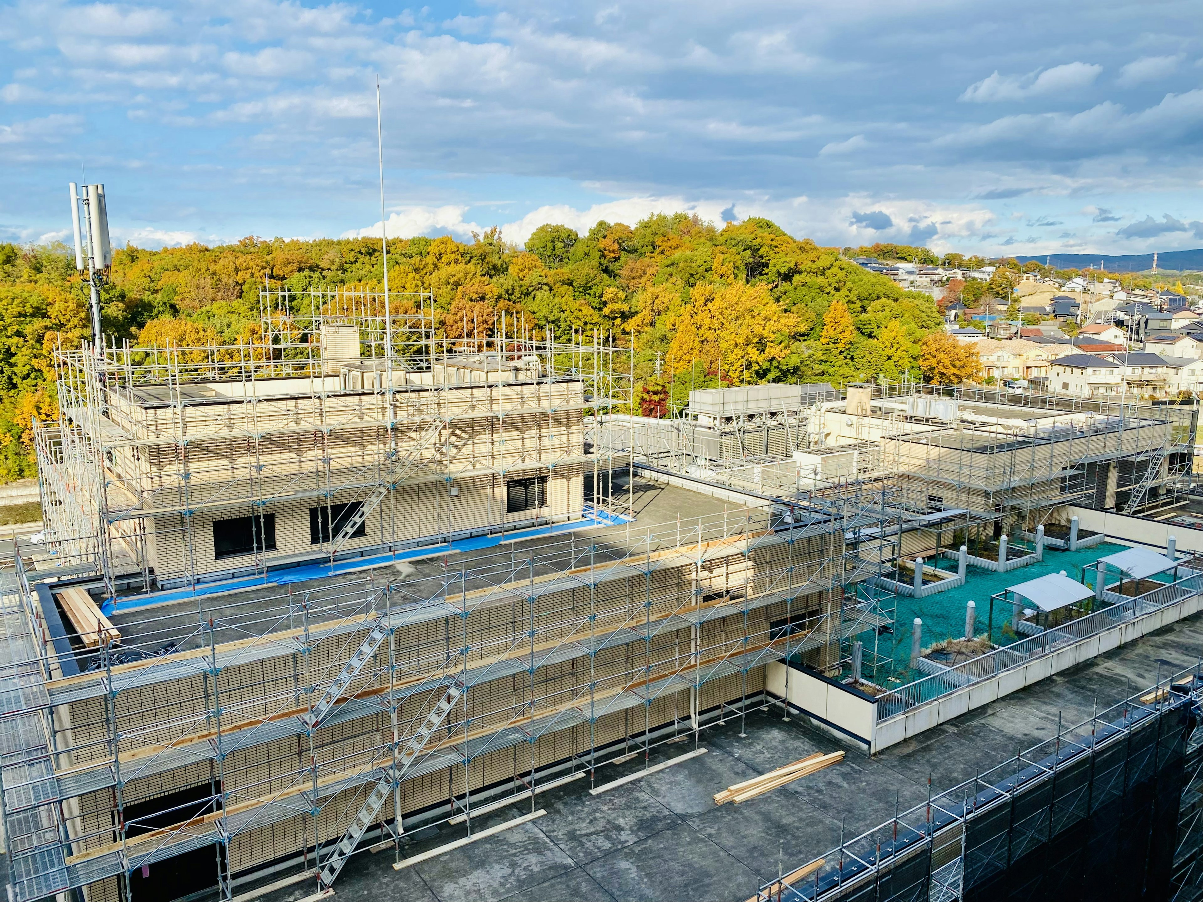 Sitio de construcción con andamios alrededor de un edificio y árboles de otoño al fondo