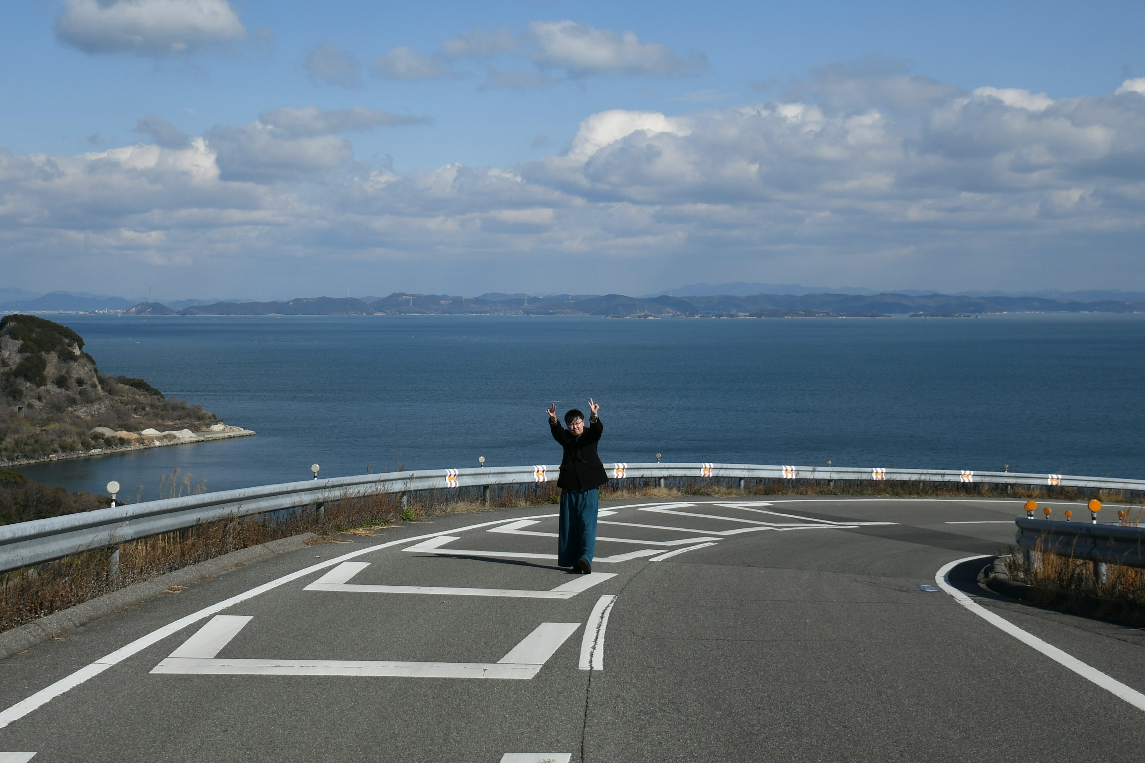 Una persona con una macchina fotografica su una strada tortuosa con vista sul mare