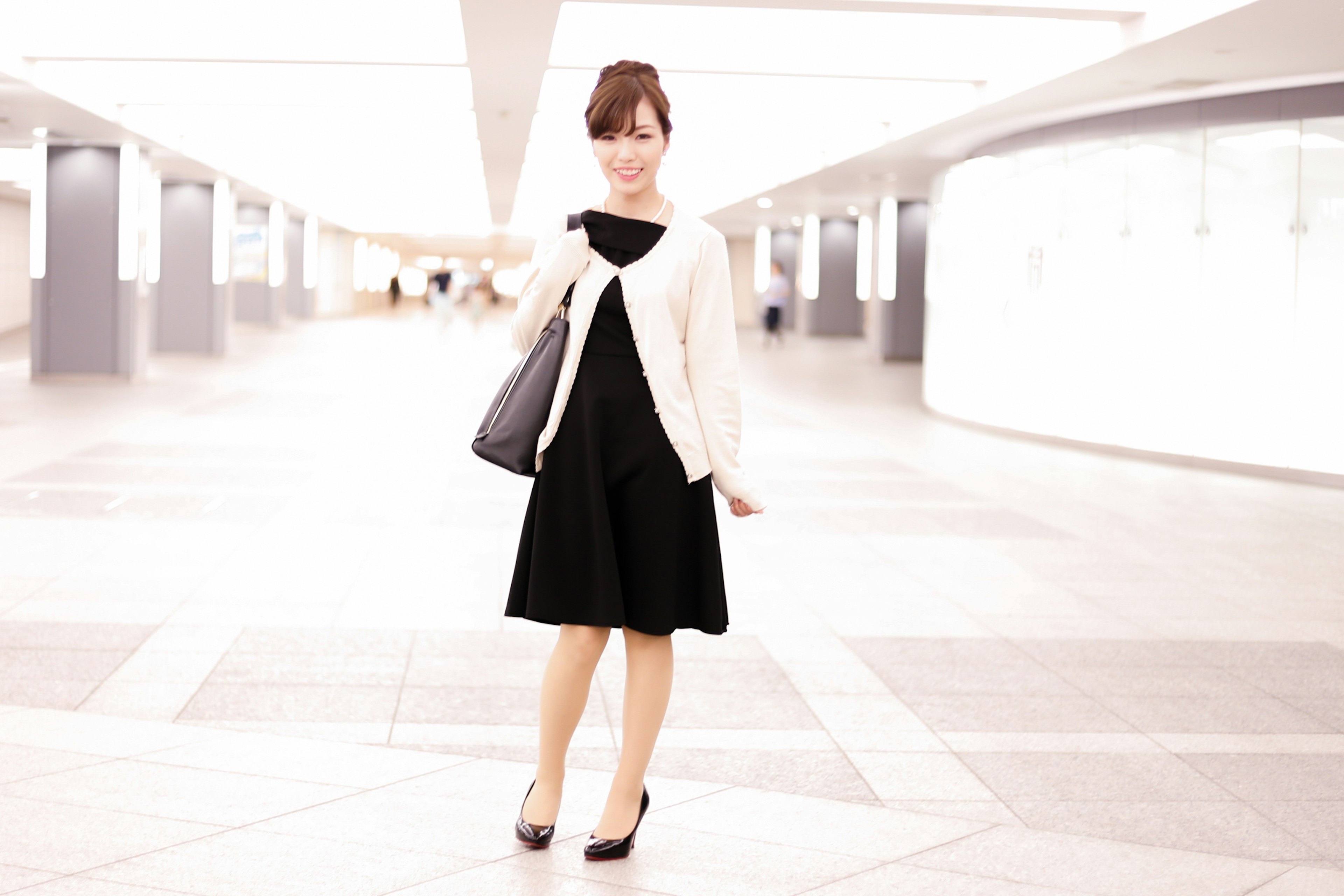 A woman in a white cardigan and black dress standing in a bright space