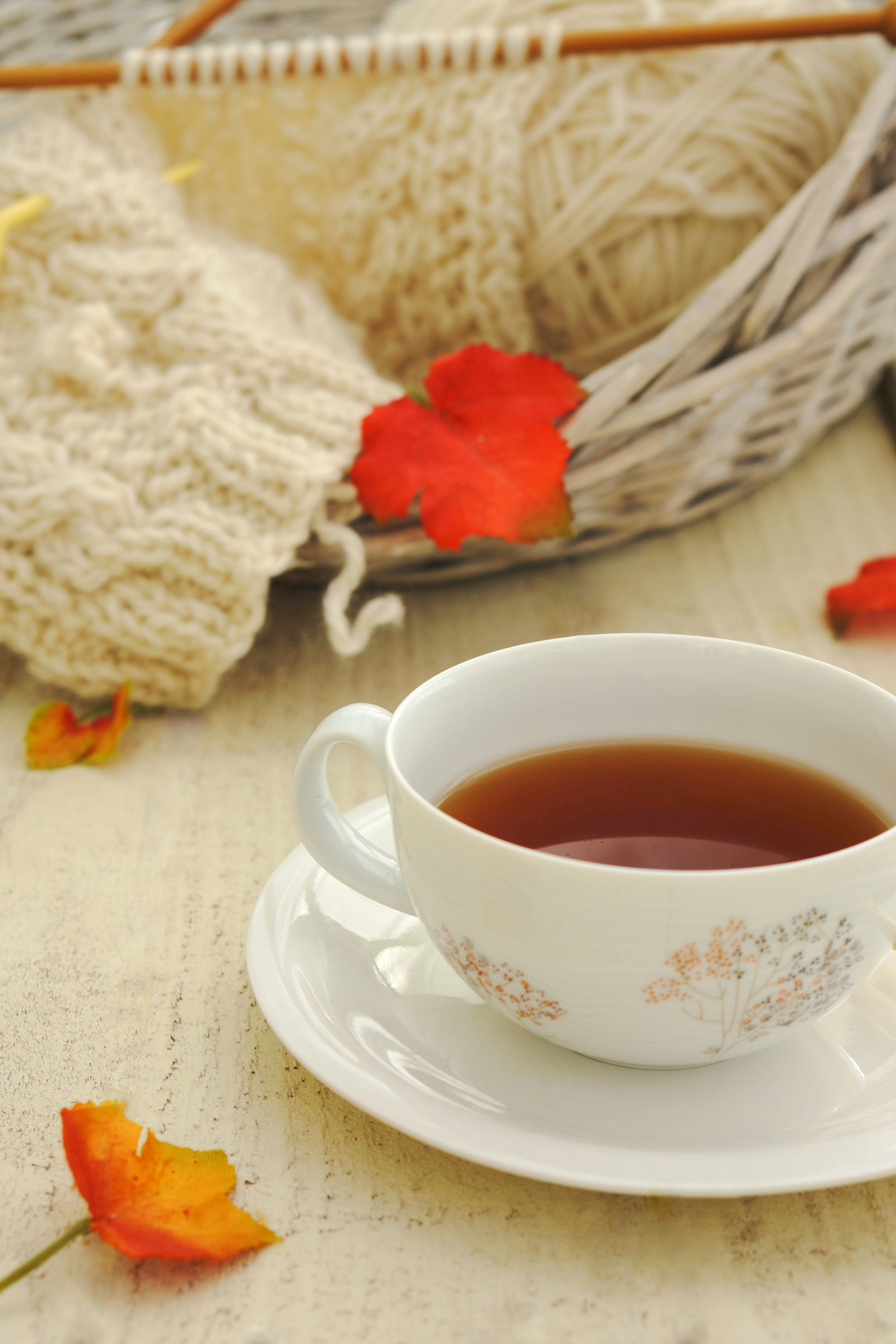 A cozy scene featuring a cup of warm tea and knitted yarn with autumn leaves