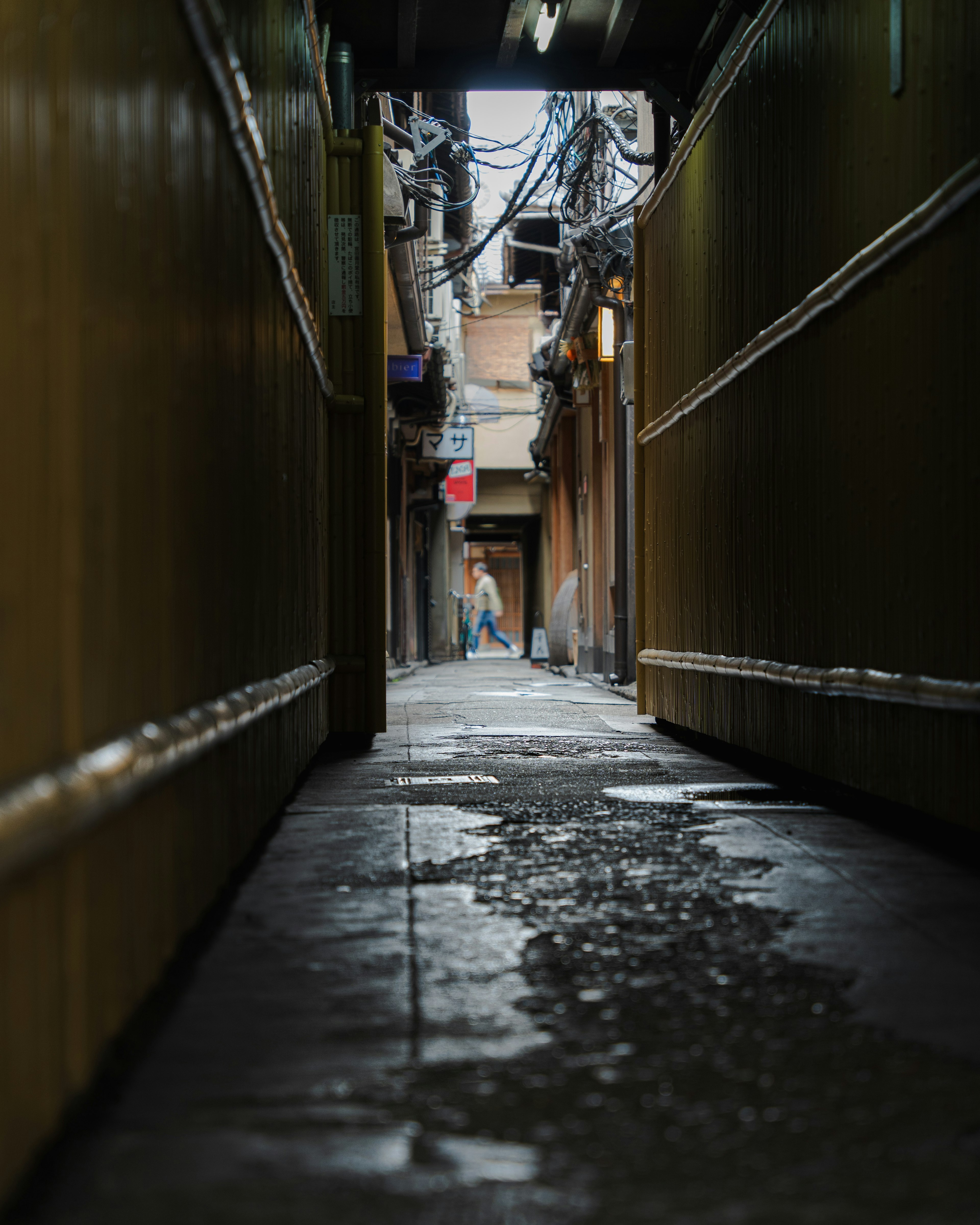 Narrow alley with puddles and a person walking in the distance