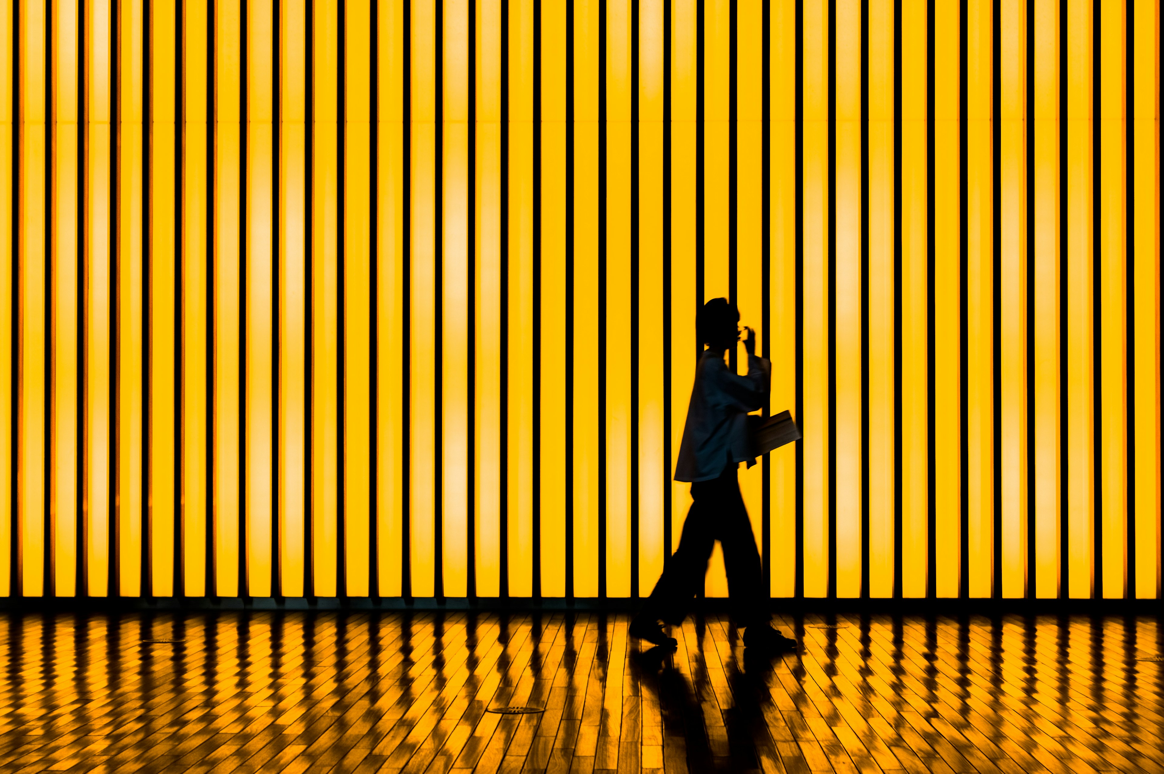 Silhouette of a person walking in front of a yellow background