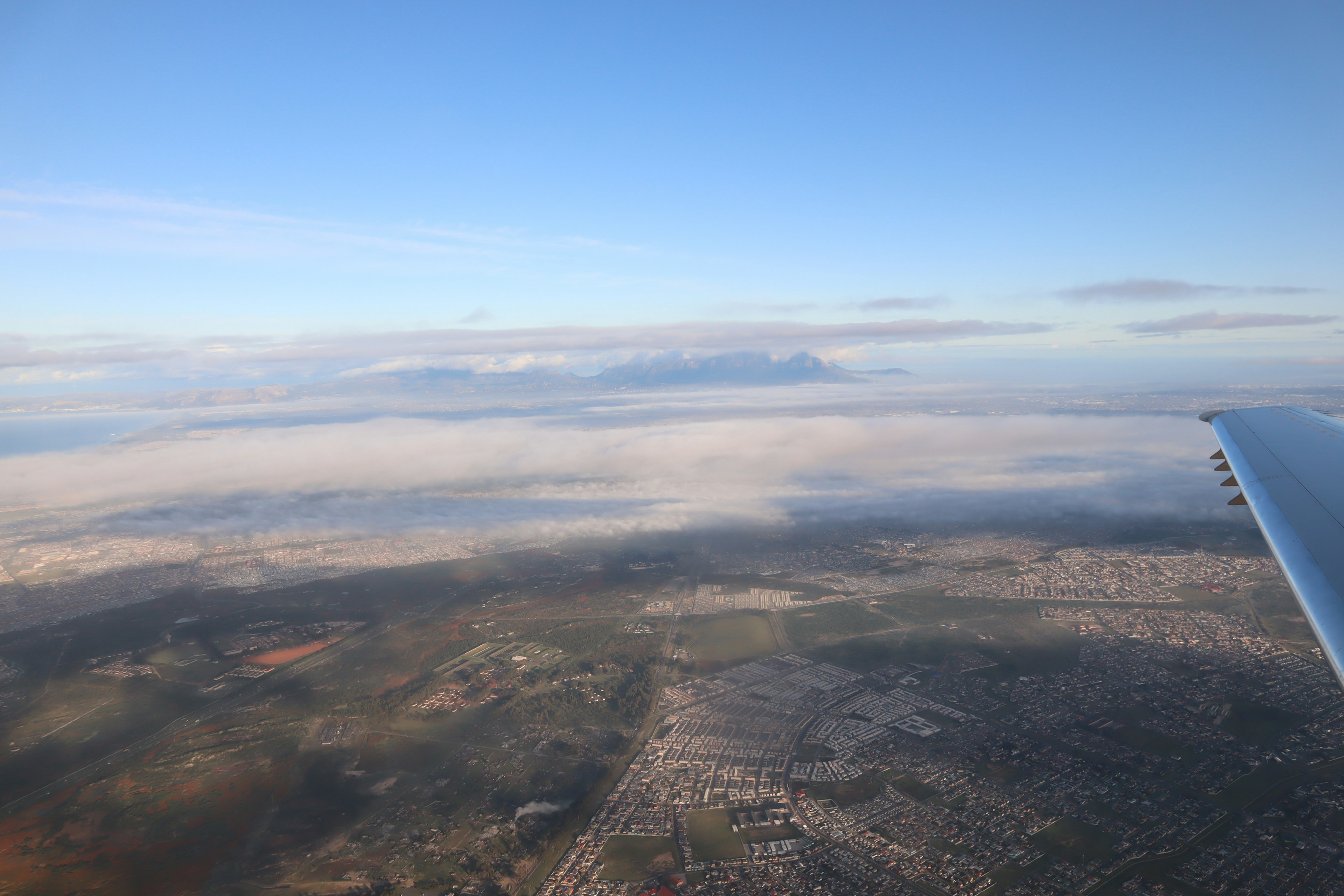 Vue aérienne depuis un avion montrant des montagnes couvertes de nuages et un paysage urbain tentaculaire