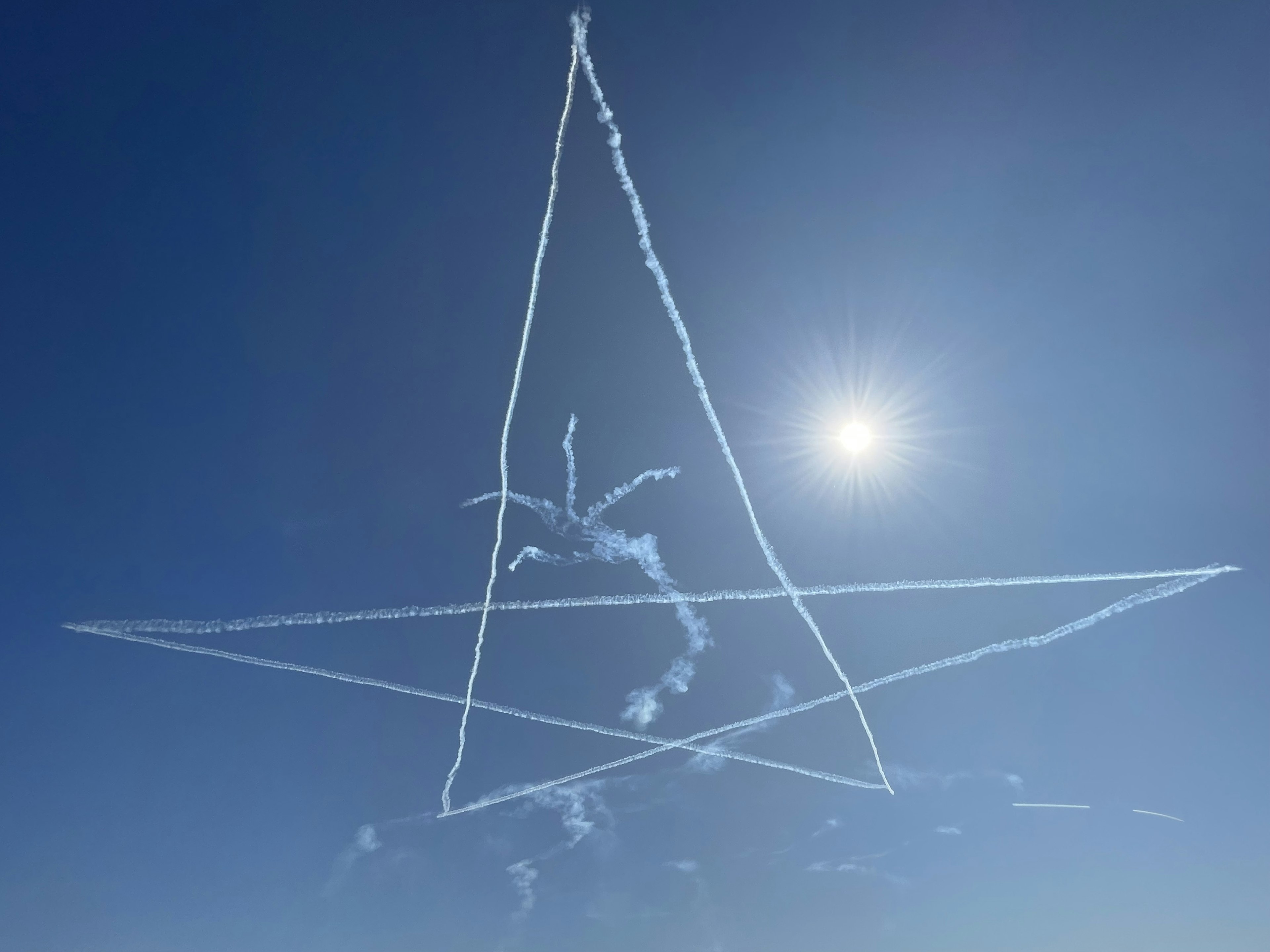 Trace de fumée en forme d'étoile dans le ciel bleu avec le soleil