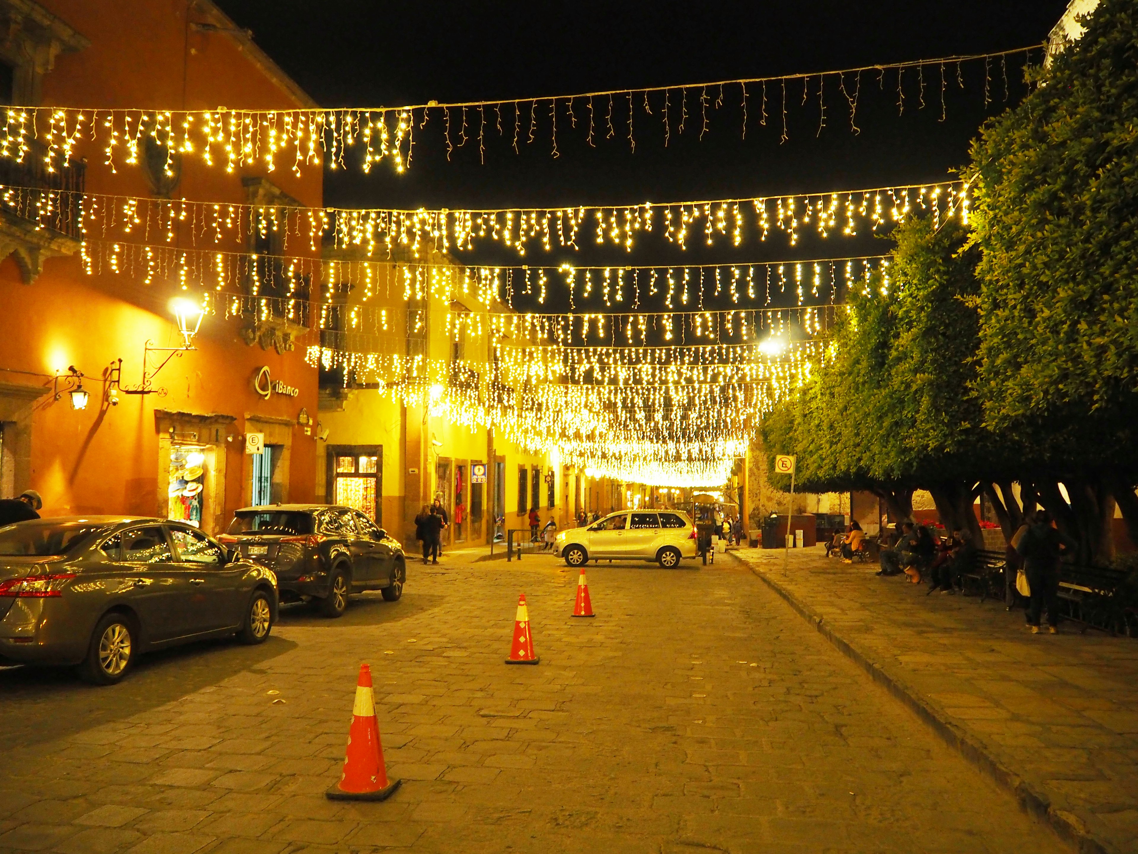 Calle nocturna adornada con luces brillantes y coches estacionados