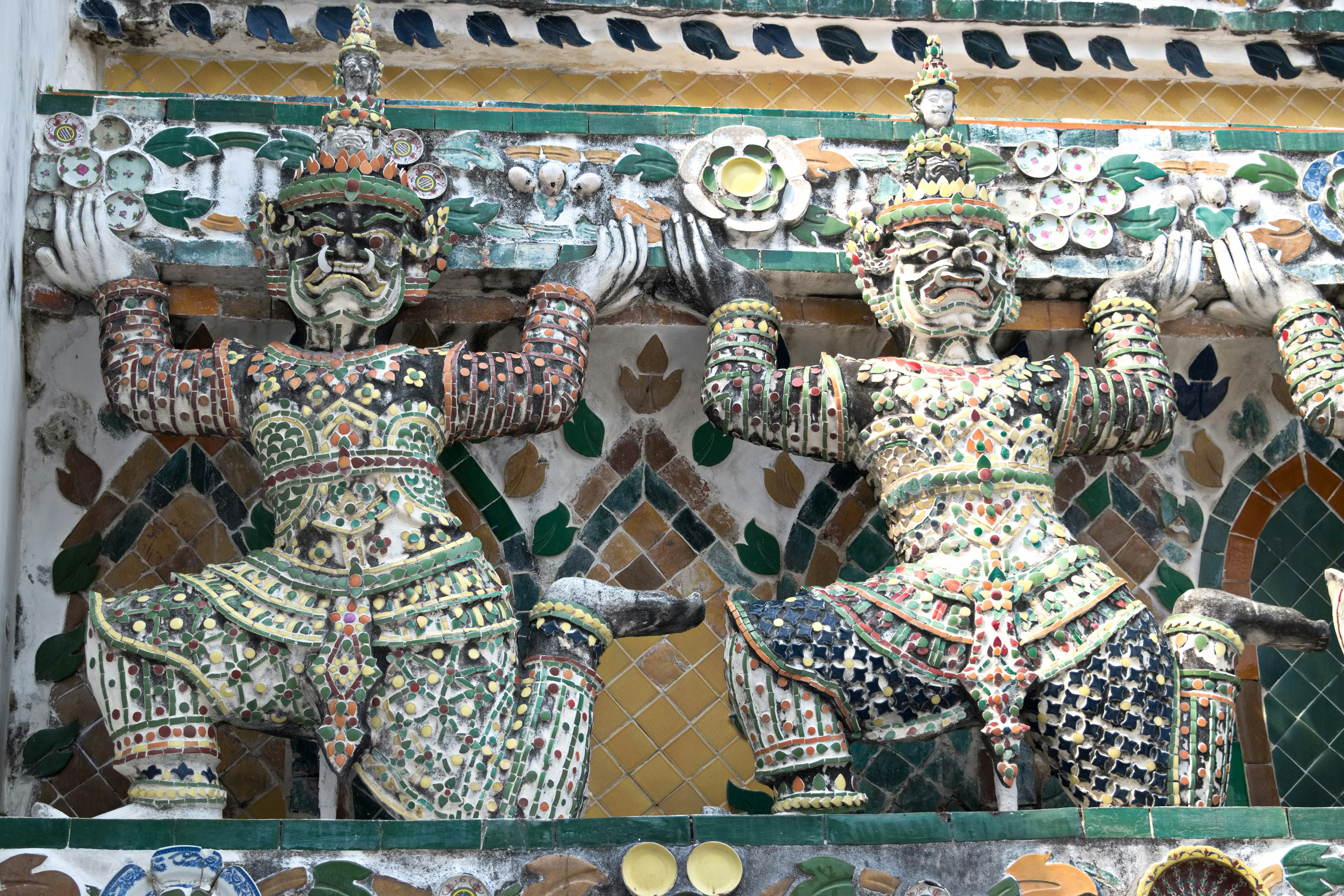 Two decorative guardian statues lifting a structure with intricate carvings and colorful tiles