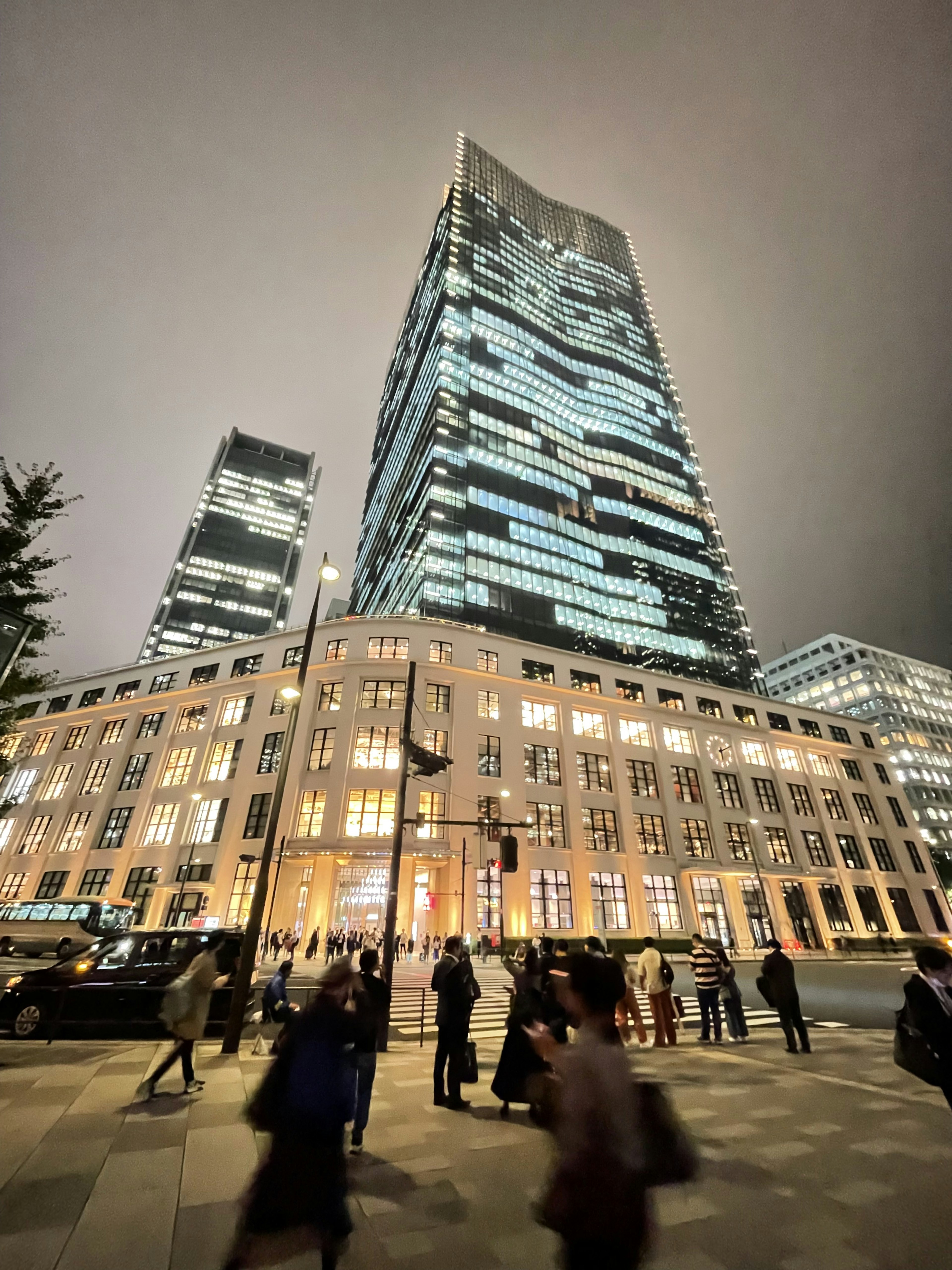 City scene featuring tall skyscrapers at night with people walking