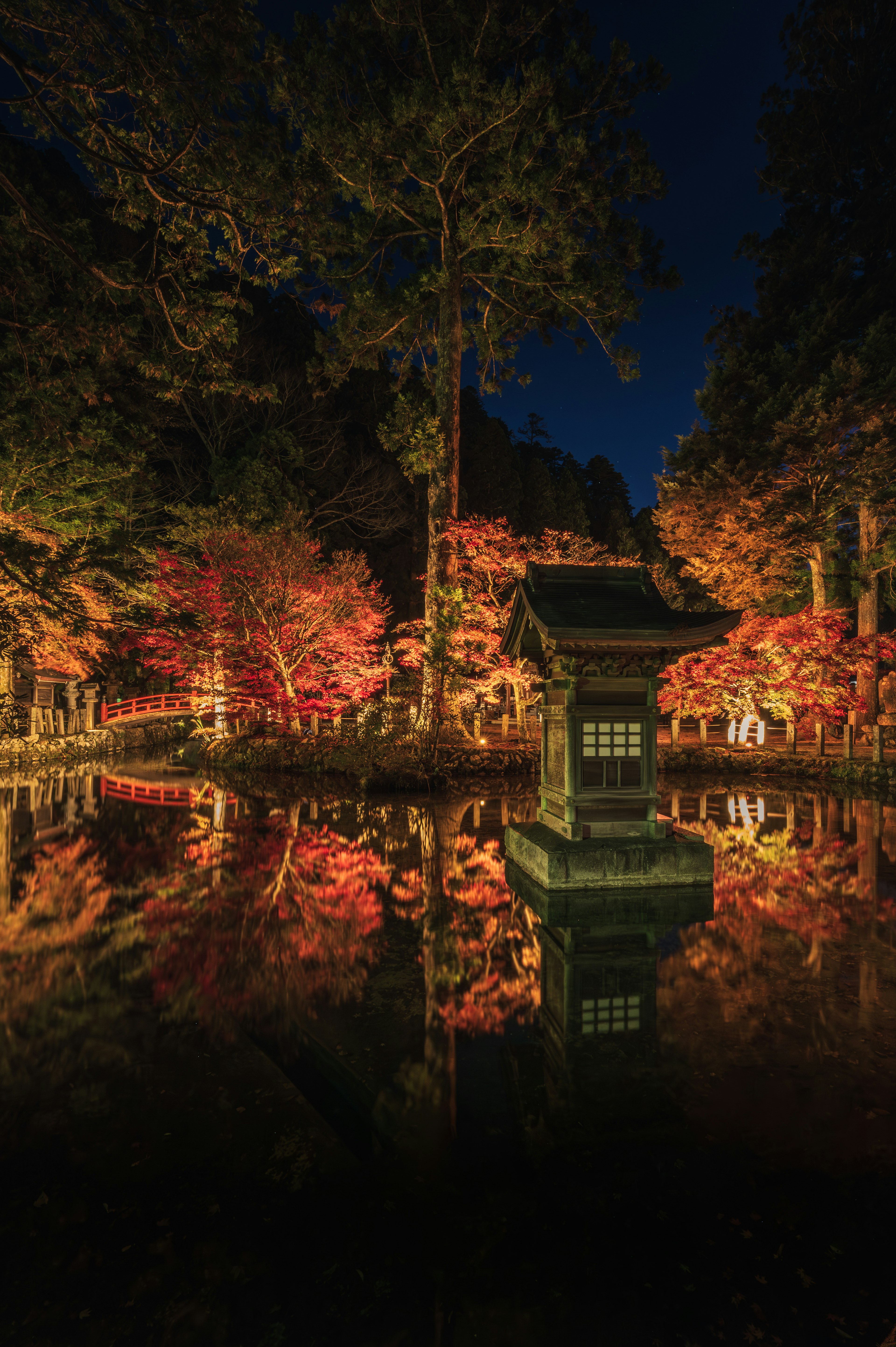 Hermoso follaje de otoño y un pequeño edificio reflejados en un estanque nocturno