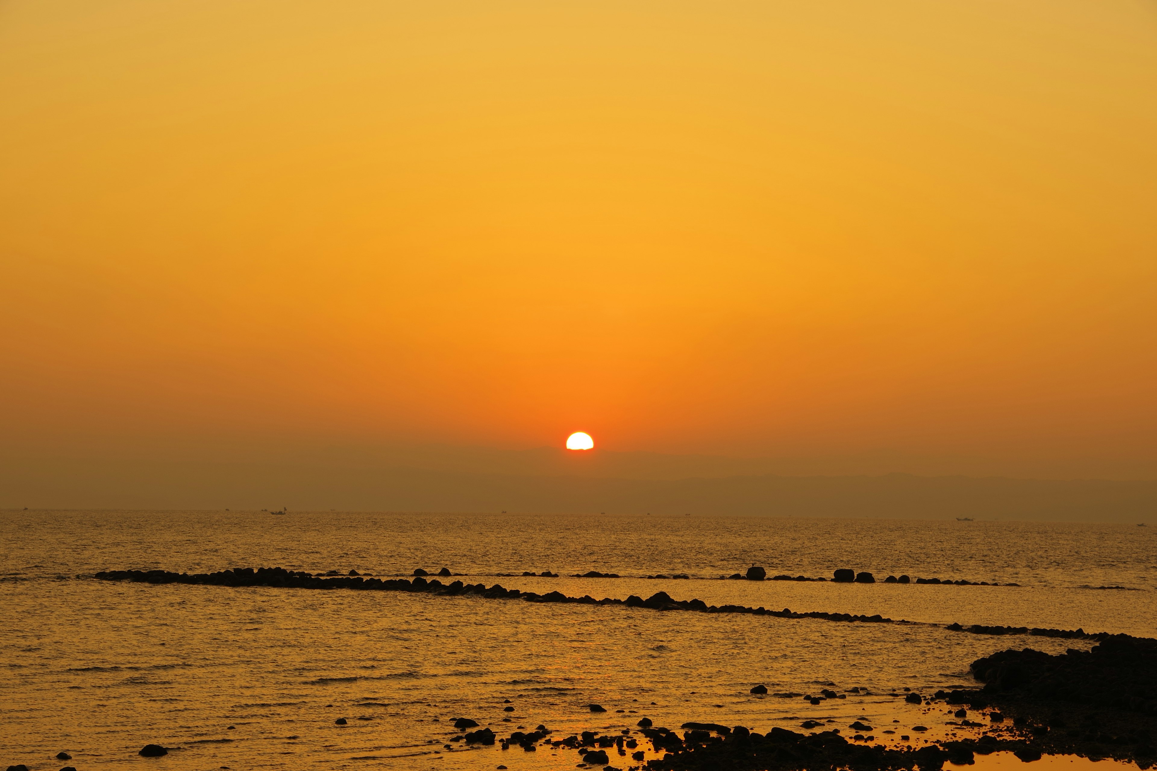 Oranger Sonnenuntergang über dem Meer mit Silhouetten von Felsen