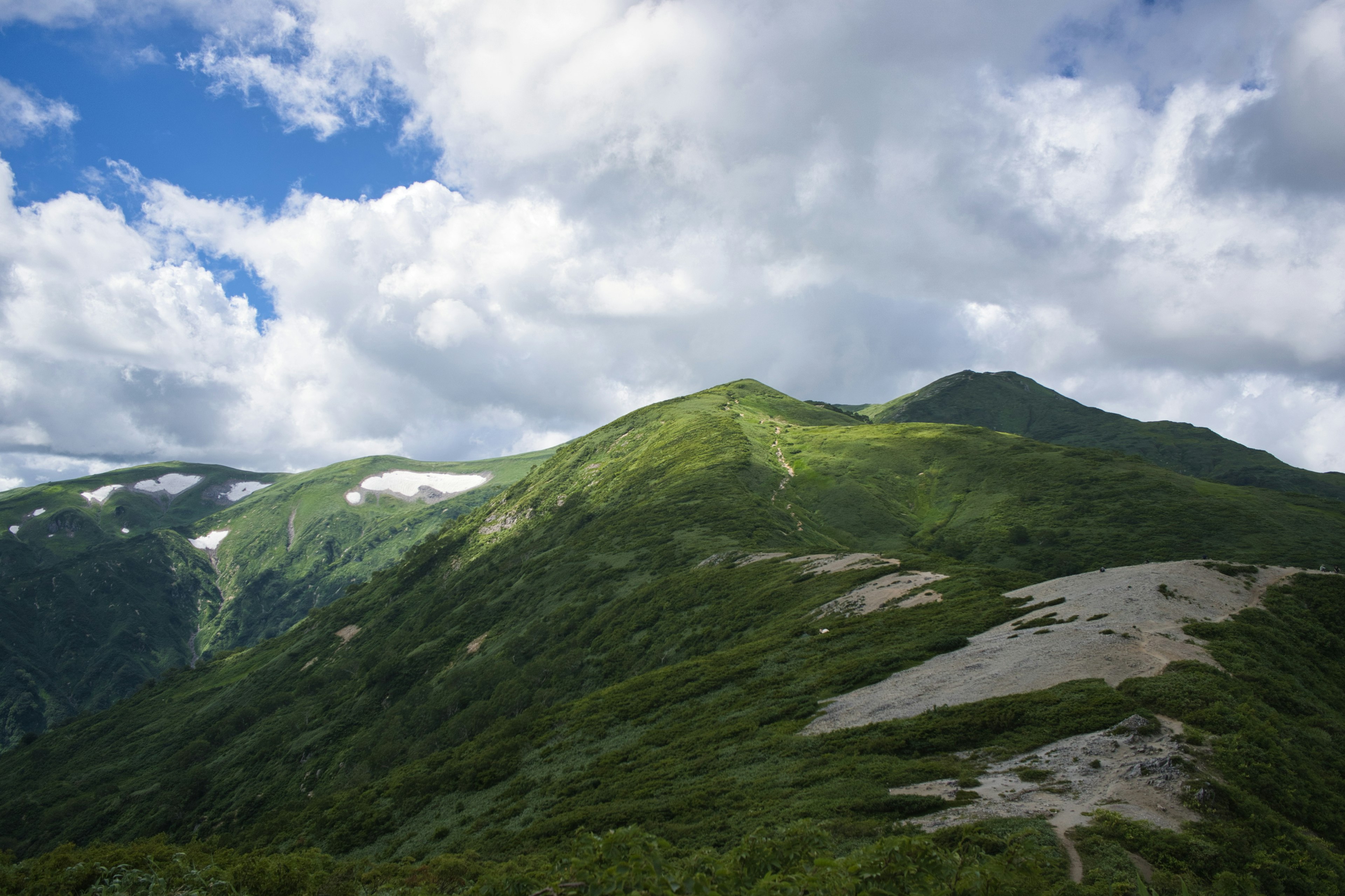 Montagne verdi sotto un cielo blu con nuvole bianche