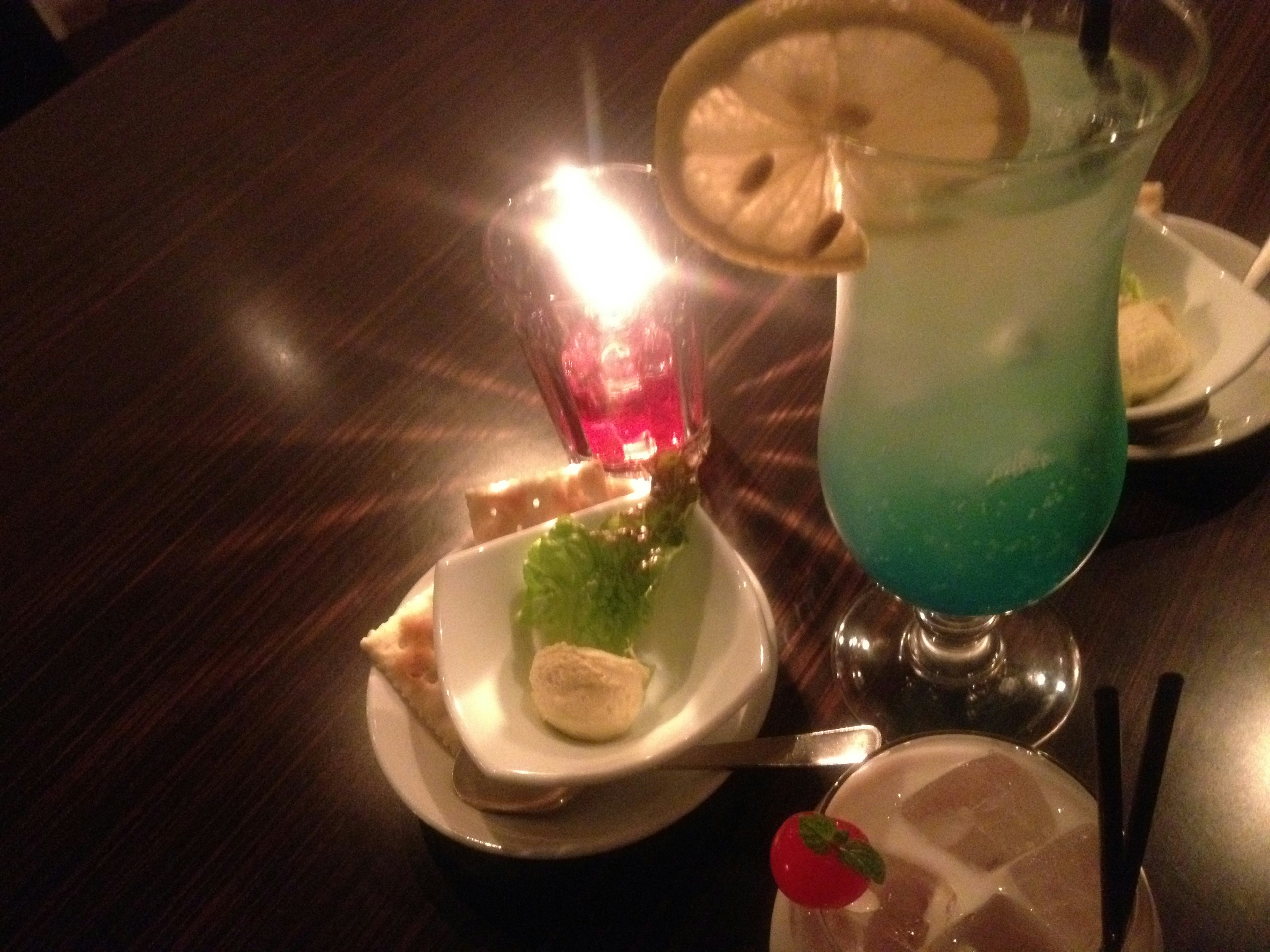 Tavolo con cocktail blu e piatto di dessert illuminato dalla luce di una candela