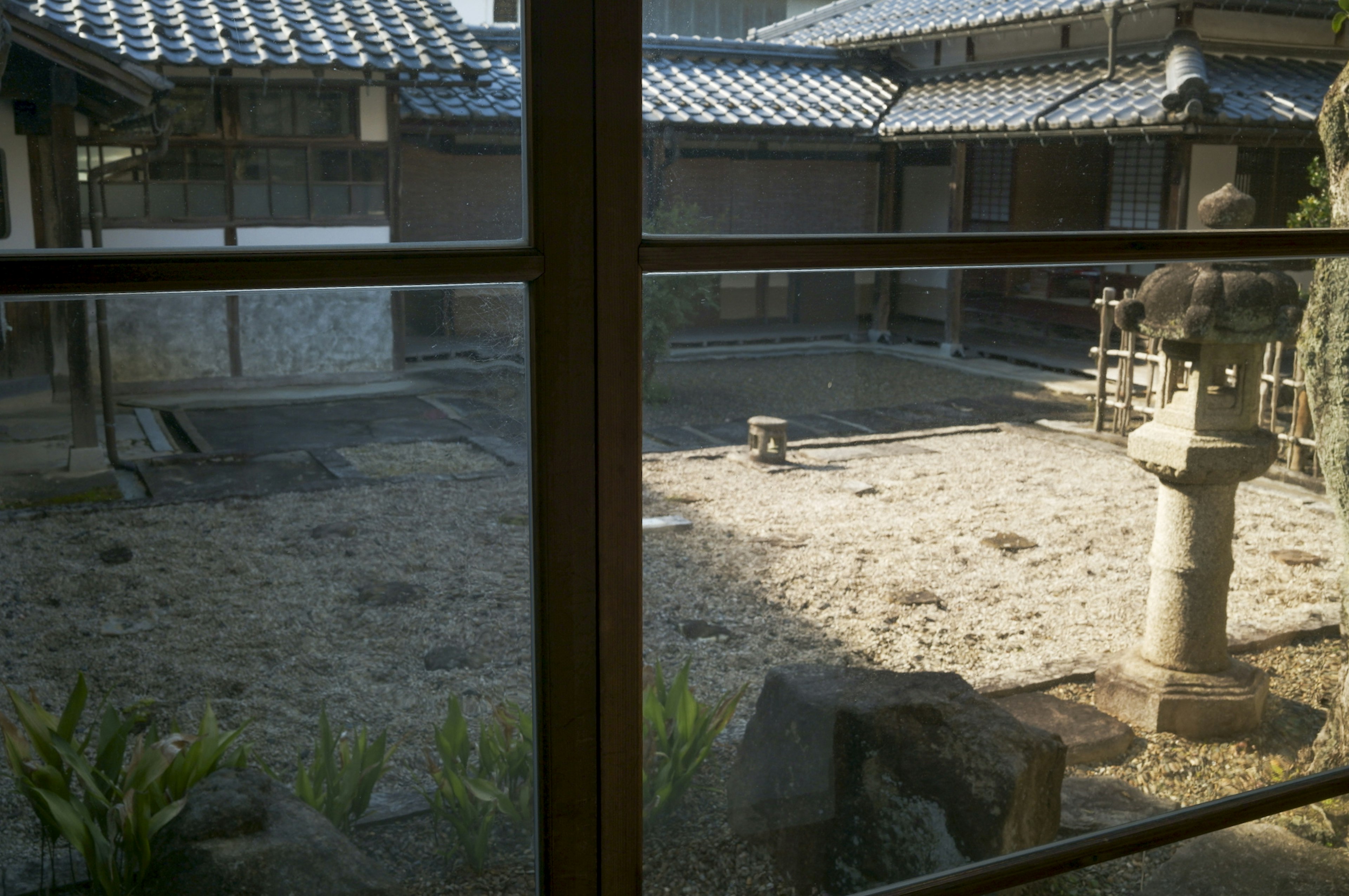 Blick durch ein Fenster auf einen traditionellen japanischen Garten mit einer Steinlaterne und einem sorgfältig geharkten Kiesbereich