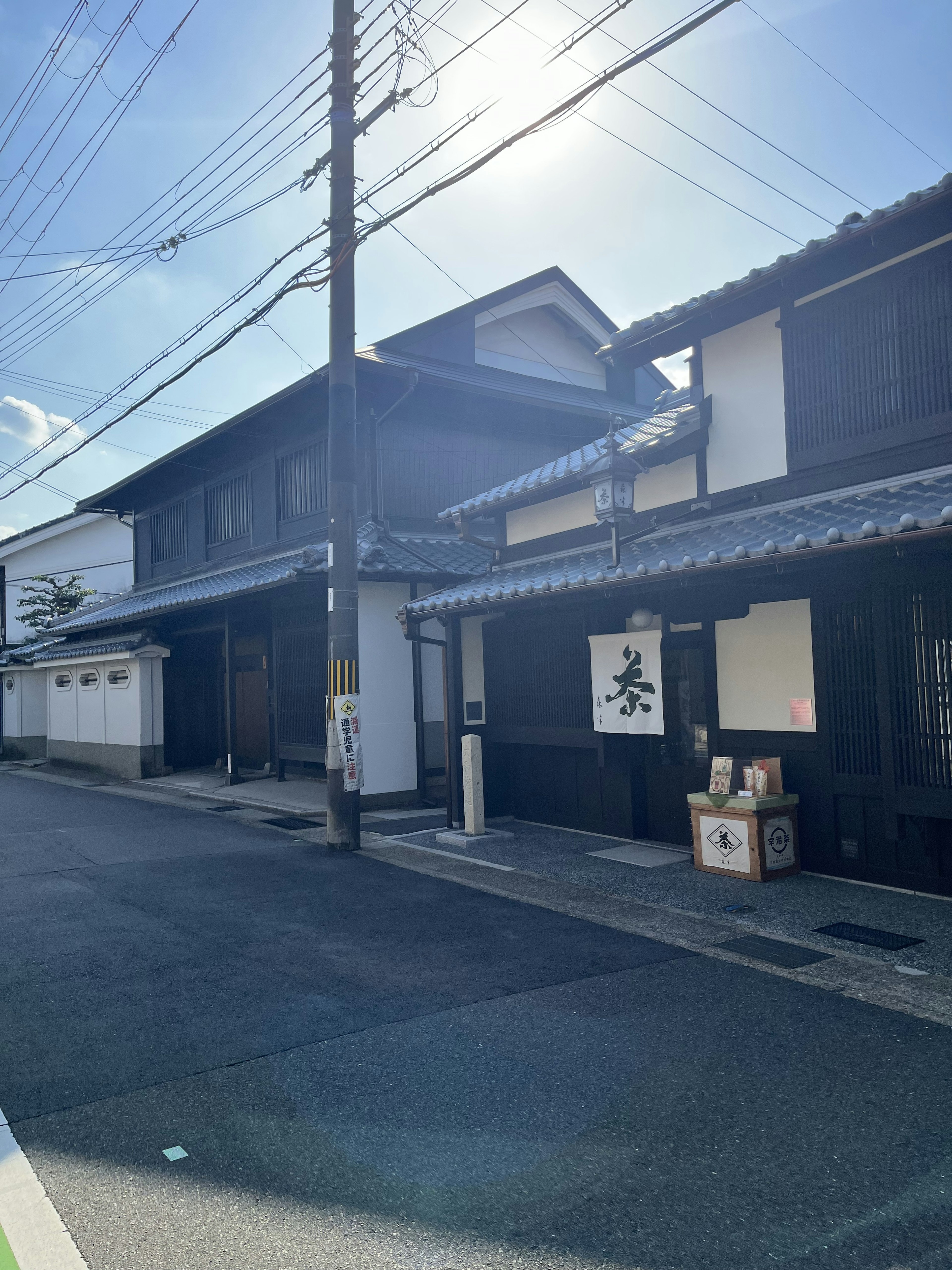 黒い伝統的な日本家屋が並ぶ街並みで、青空と太陽が輝いている