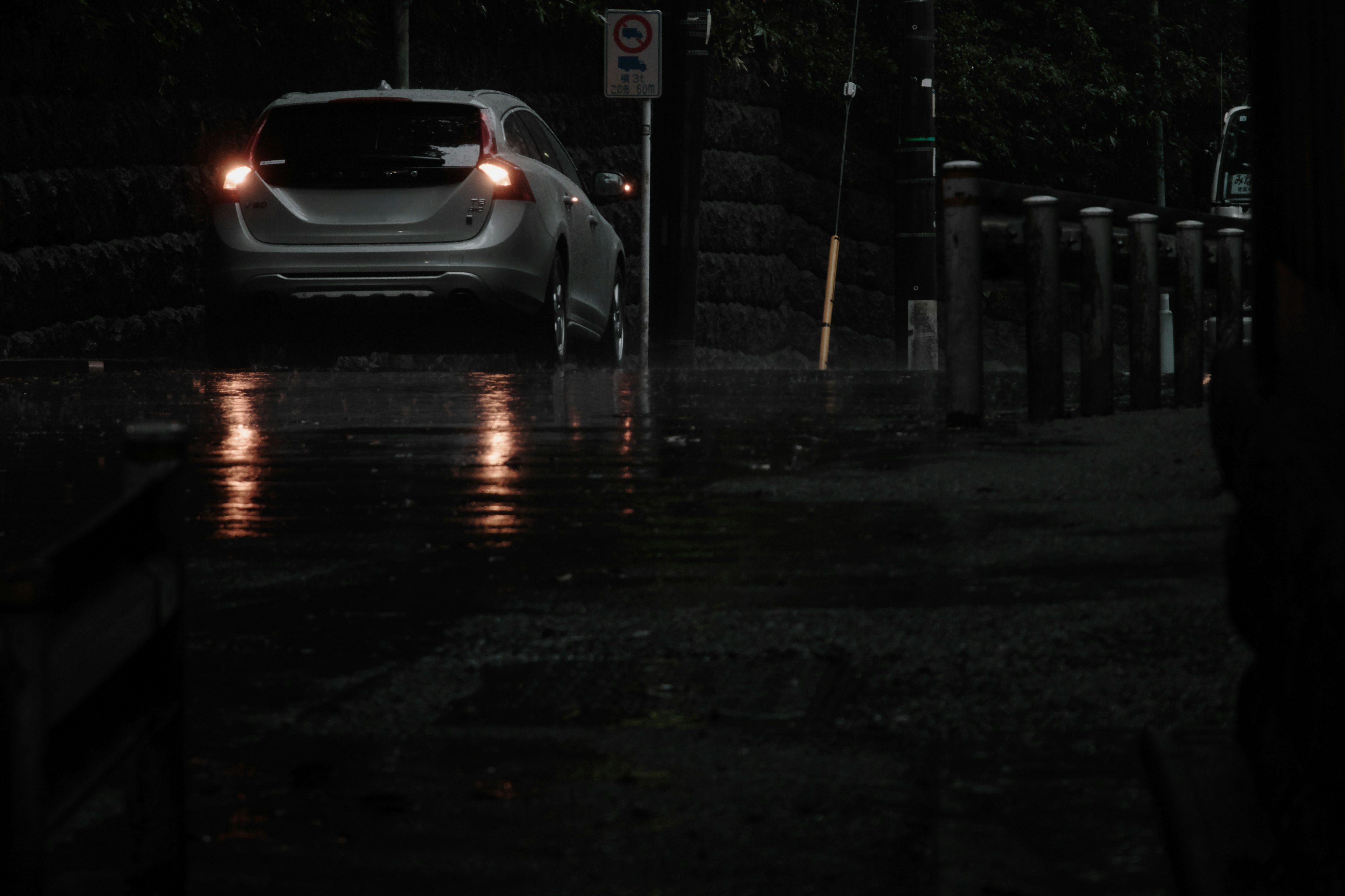 A car on a dark street with rain and reflective puddles