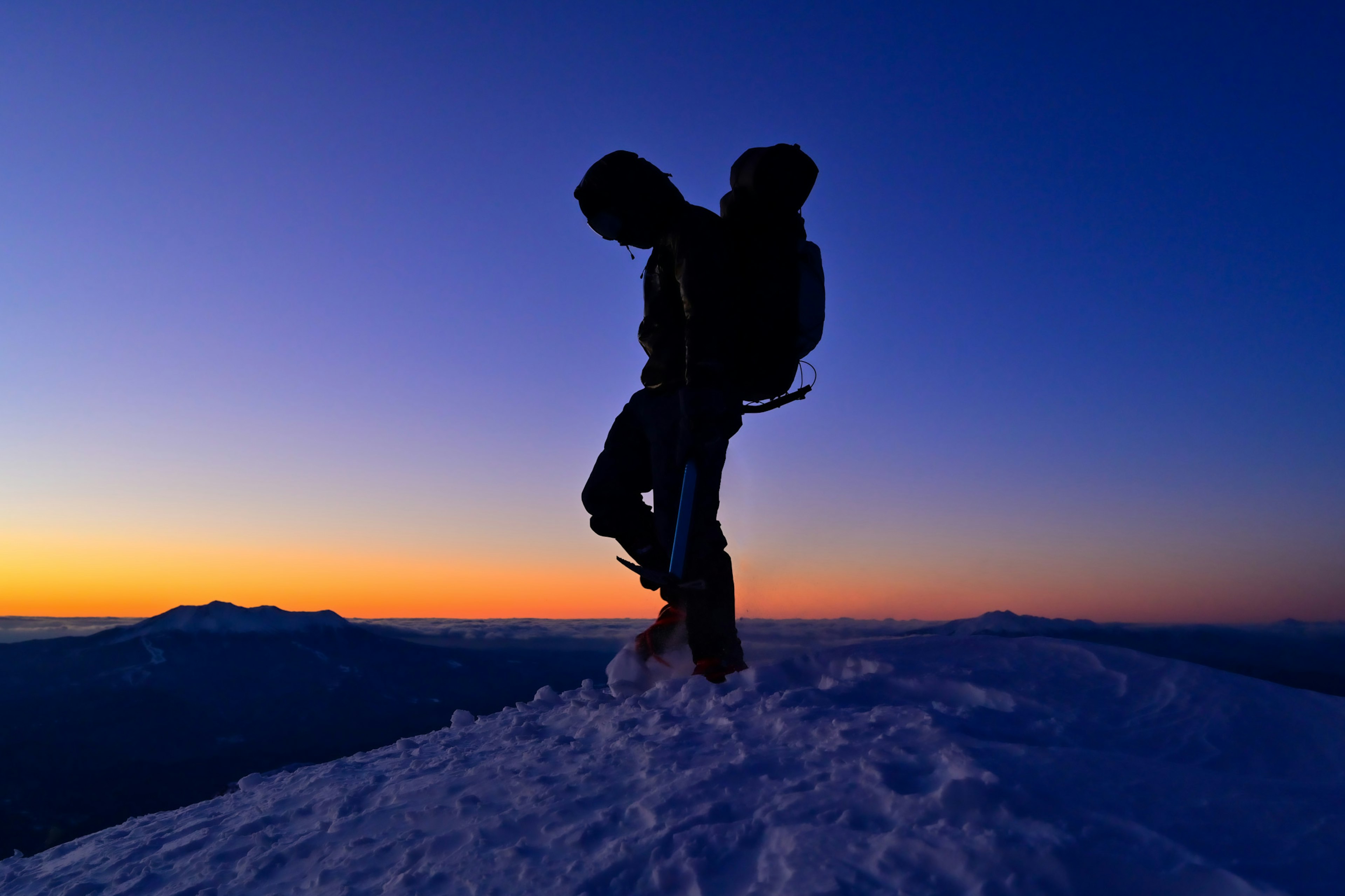 Silhouette eines Kletterers, der auf einem verschneiten Gipfel steht, vor einem schönen Sonnenuntergang