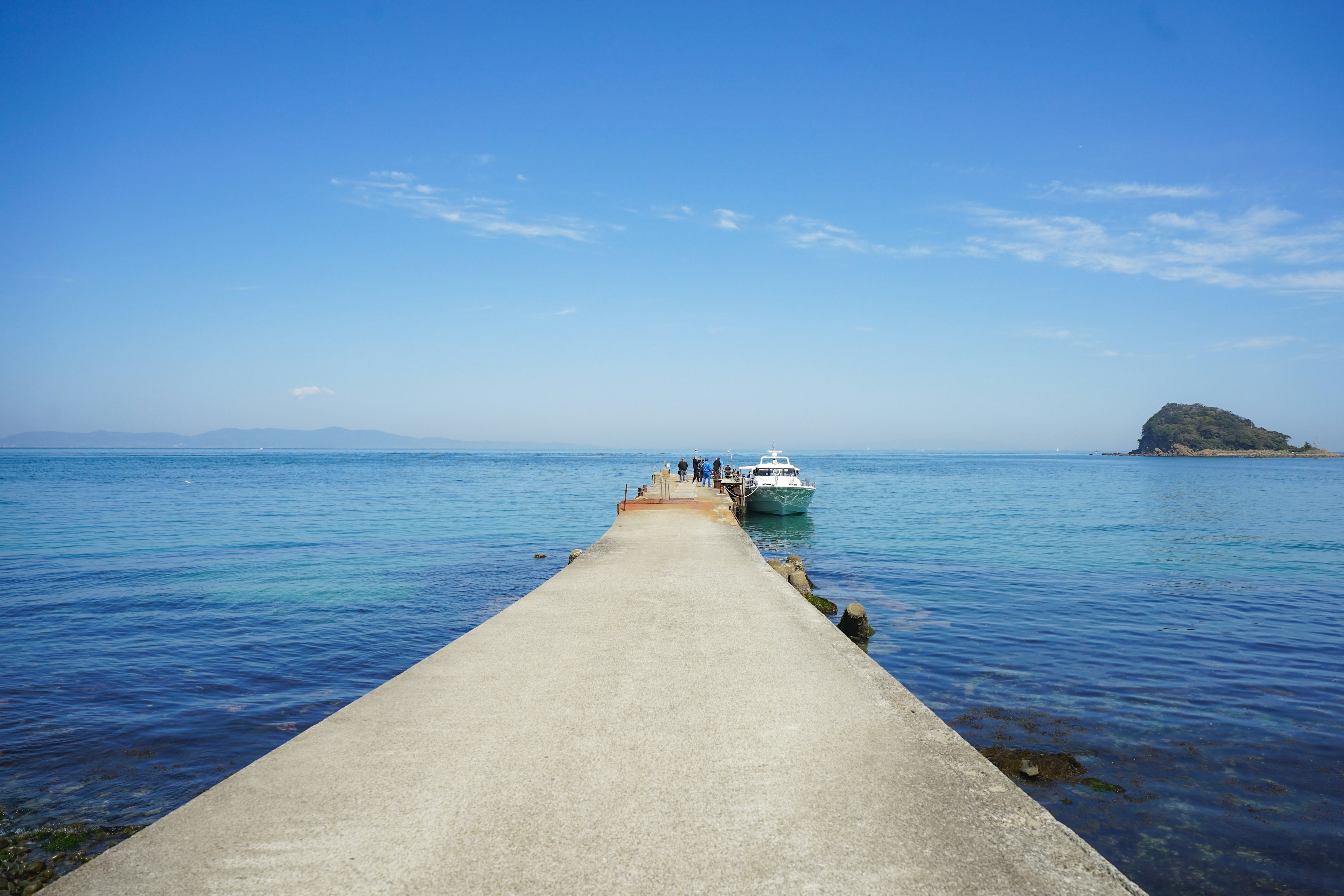 Quai en béton sous un ciel bleu avec une eau calme et un bateau amarré