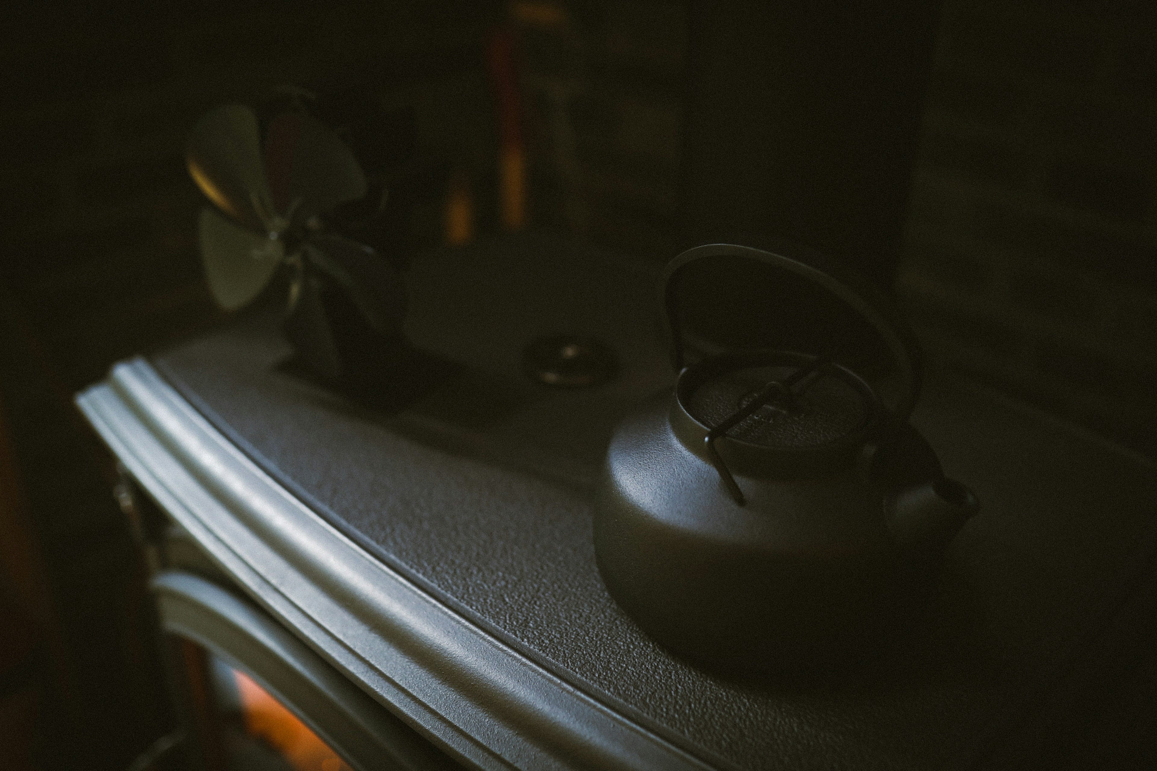 A metal kettle and a small fan placed on top of a stove in a dimly lit setting