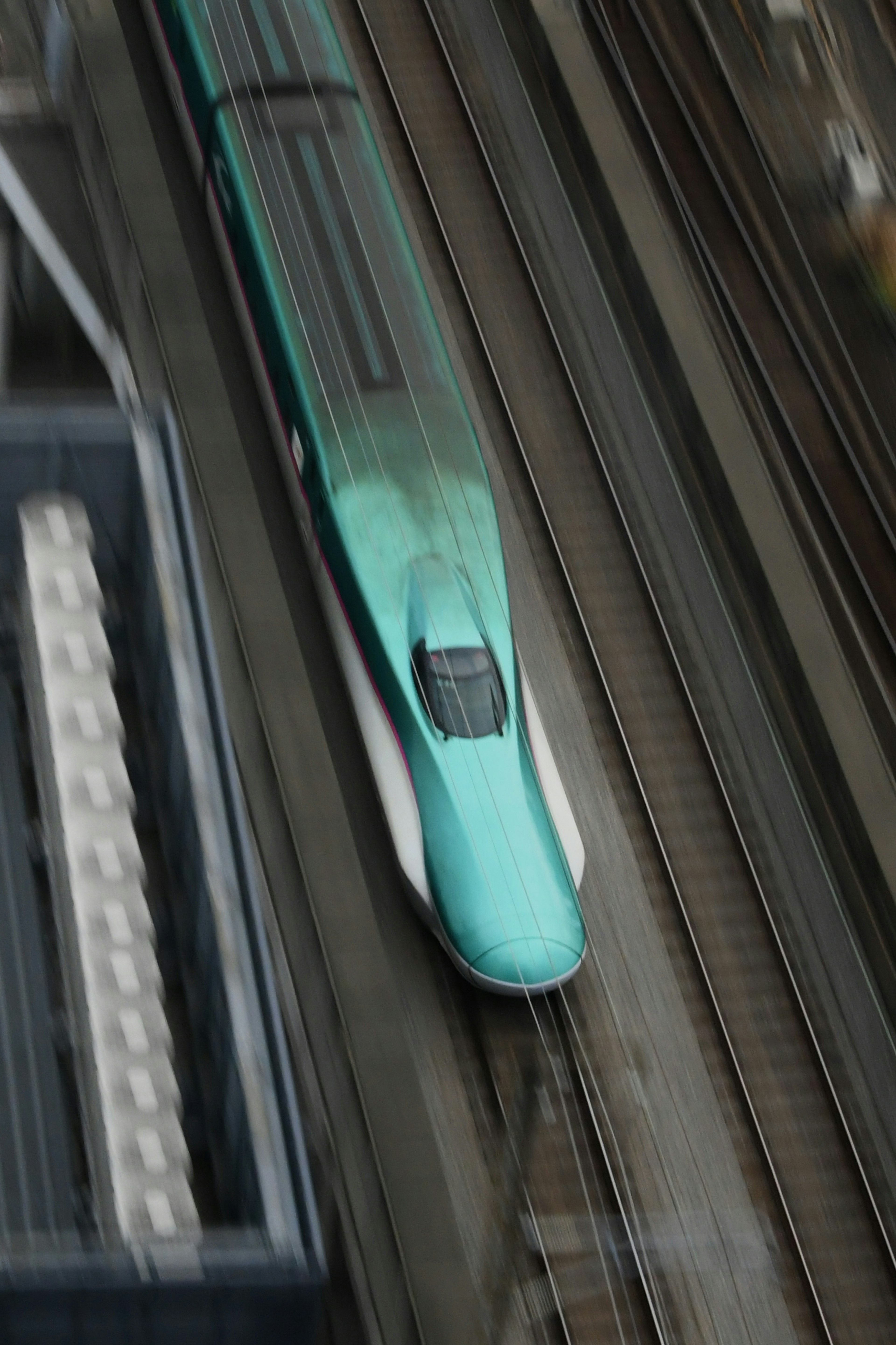 A blue Shinkansen train traveling on tracks from an overhead perspective