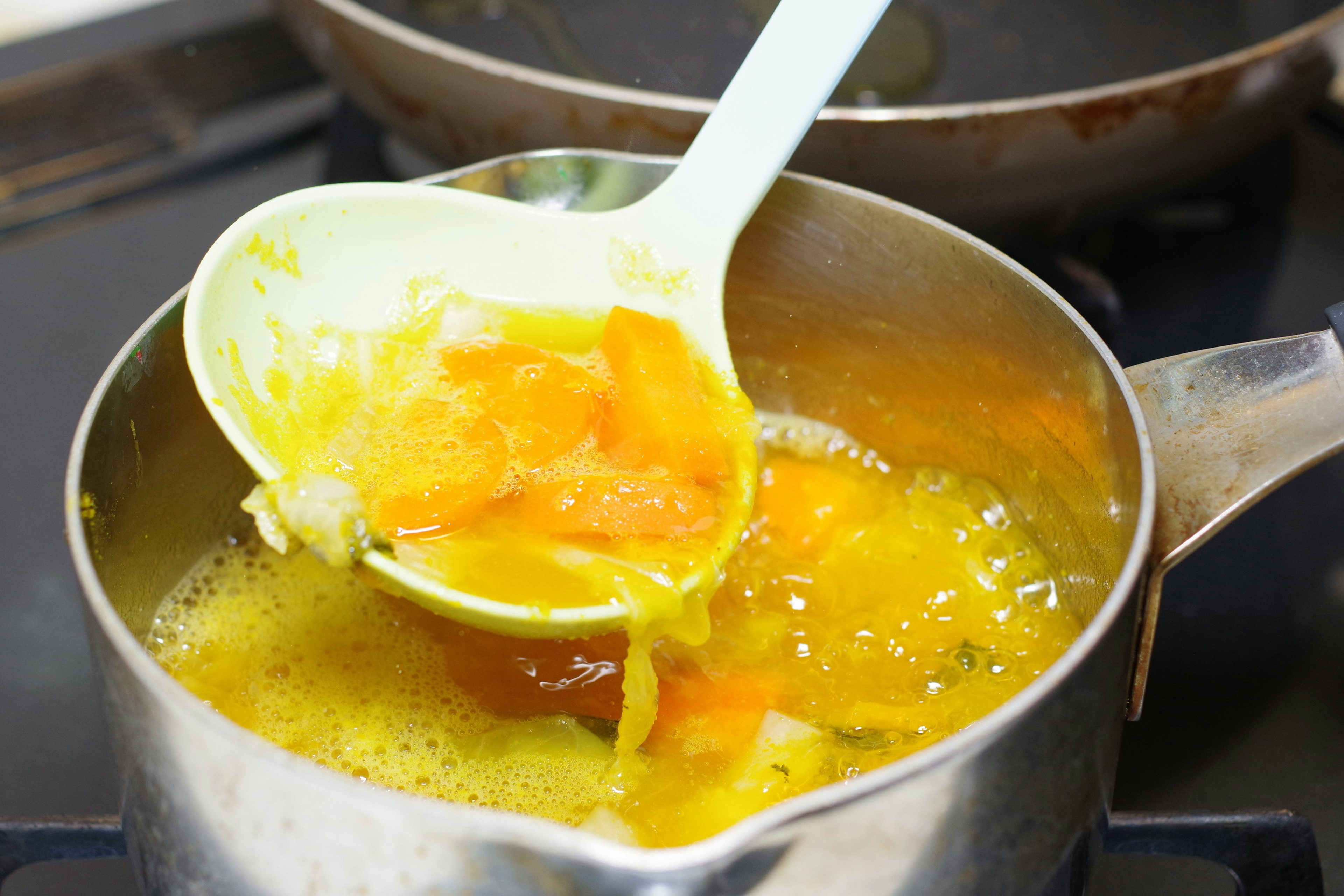 A white spoon lifting orange ingredients from a pot on the stove