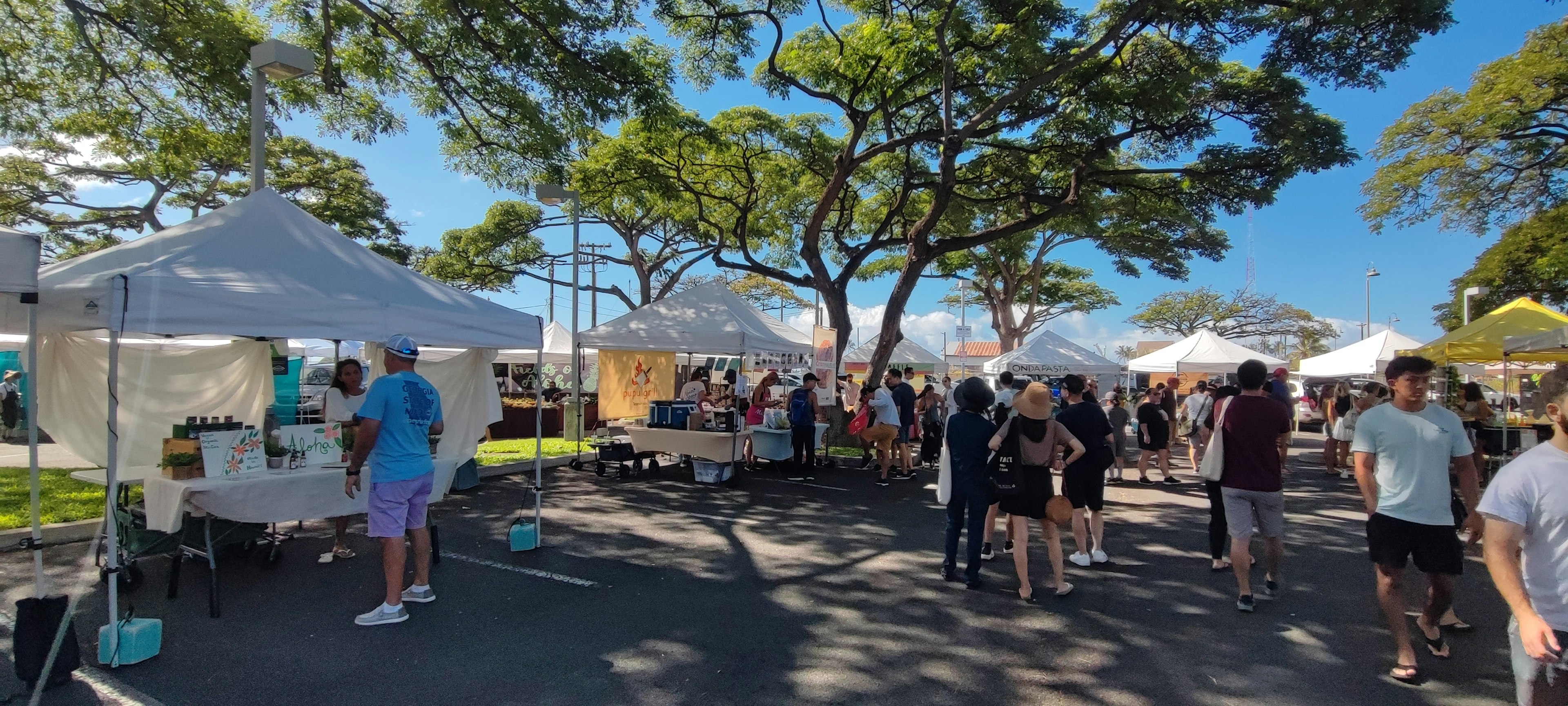 Une scène de marché animée sous un ciel bleu avec des stands et des gens rassemblés