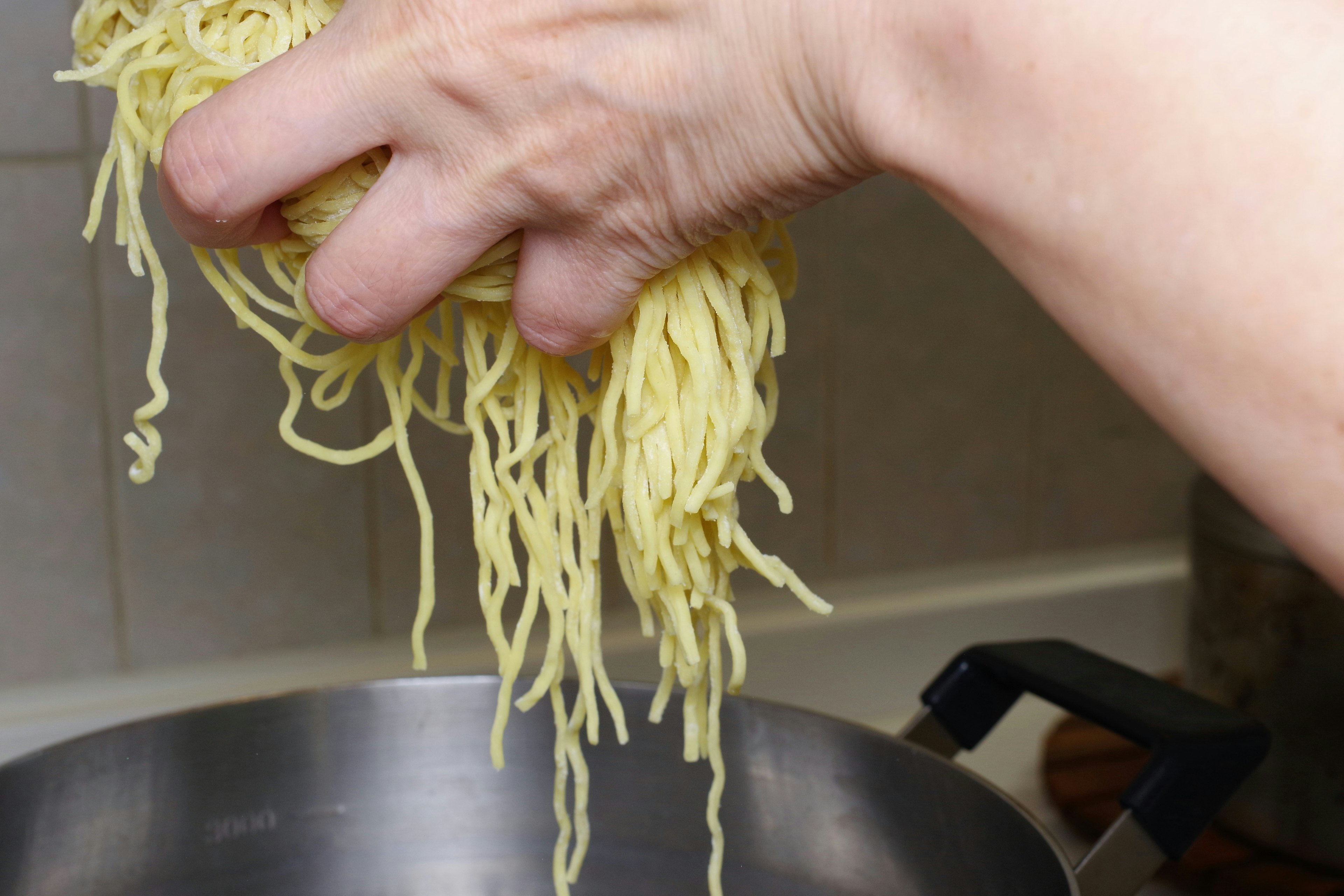 Eine Hand hält rohe Nudeln über einem Topf, bereit zum Kochen