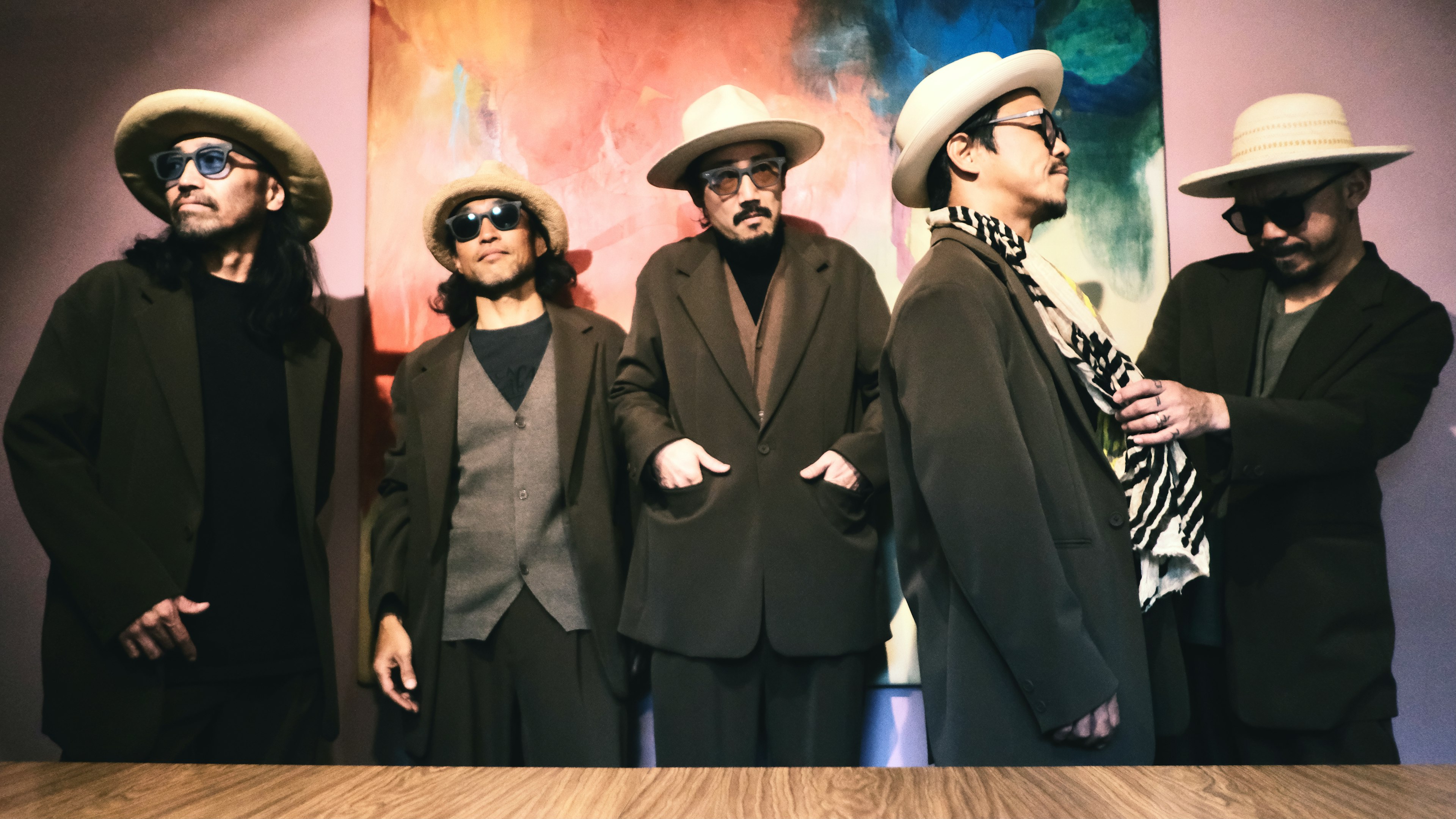 Cinco hombres con trajes elegantes usando sombreros y gafas de sol posando juntos