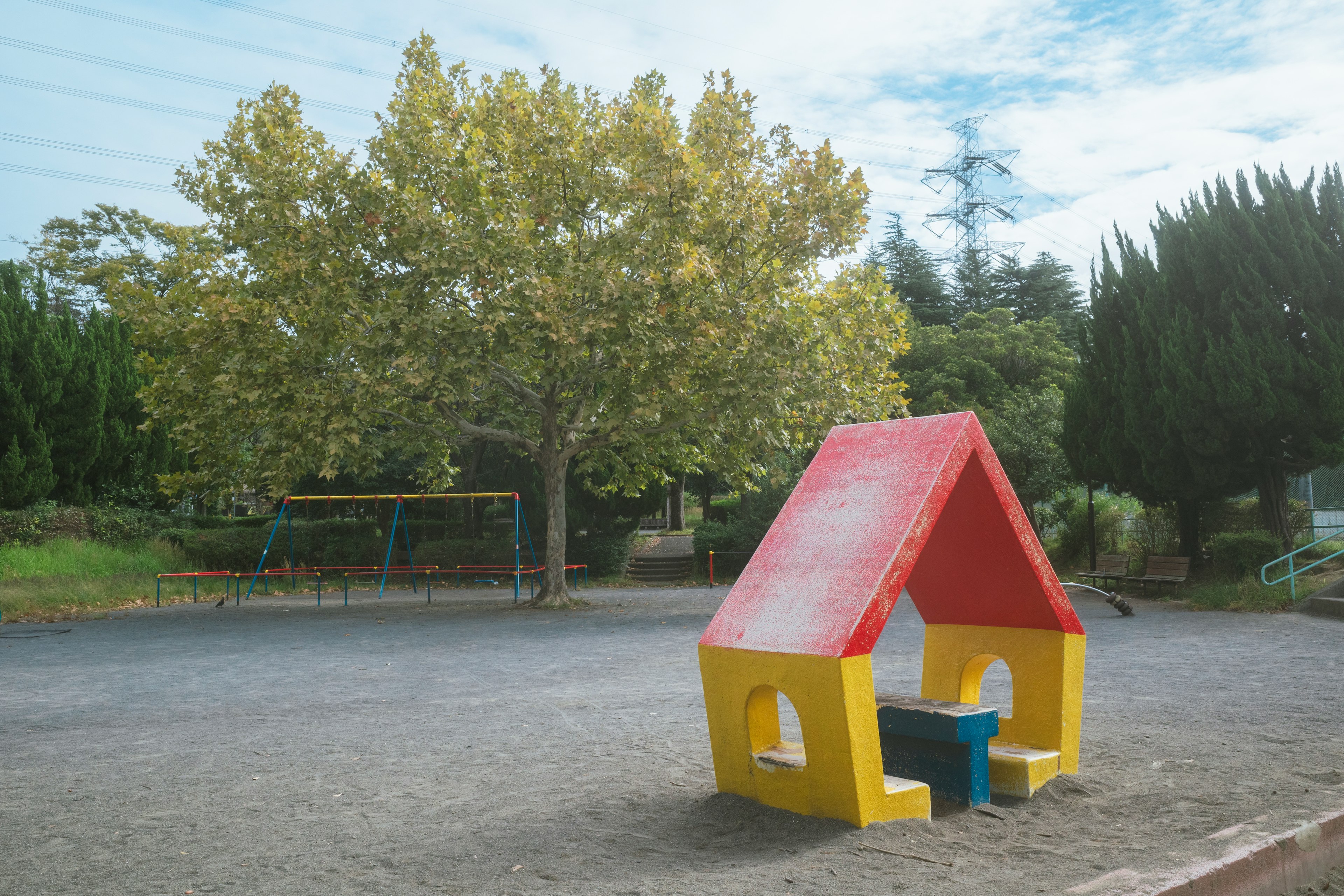 Colorful play area featuring a red and yellow playhouse and a large tree