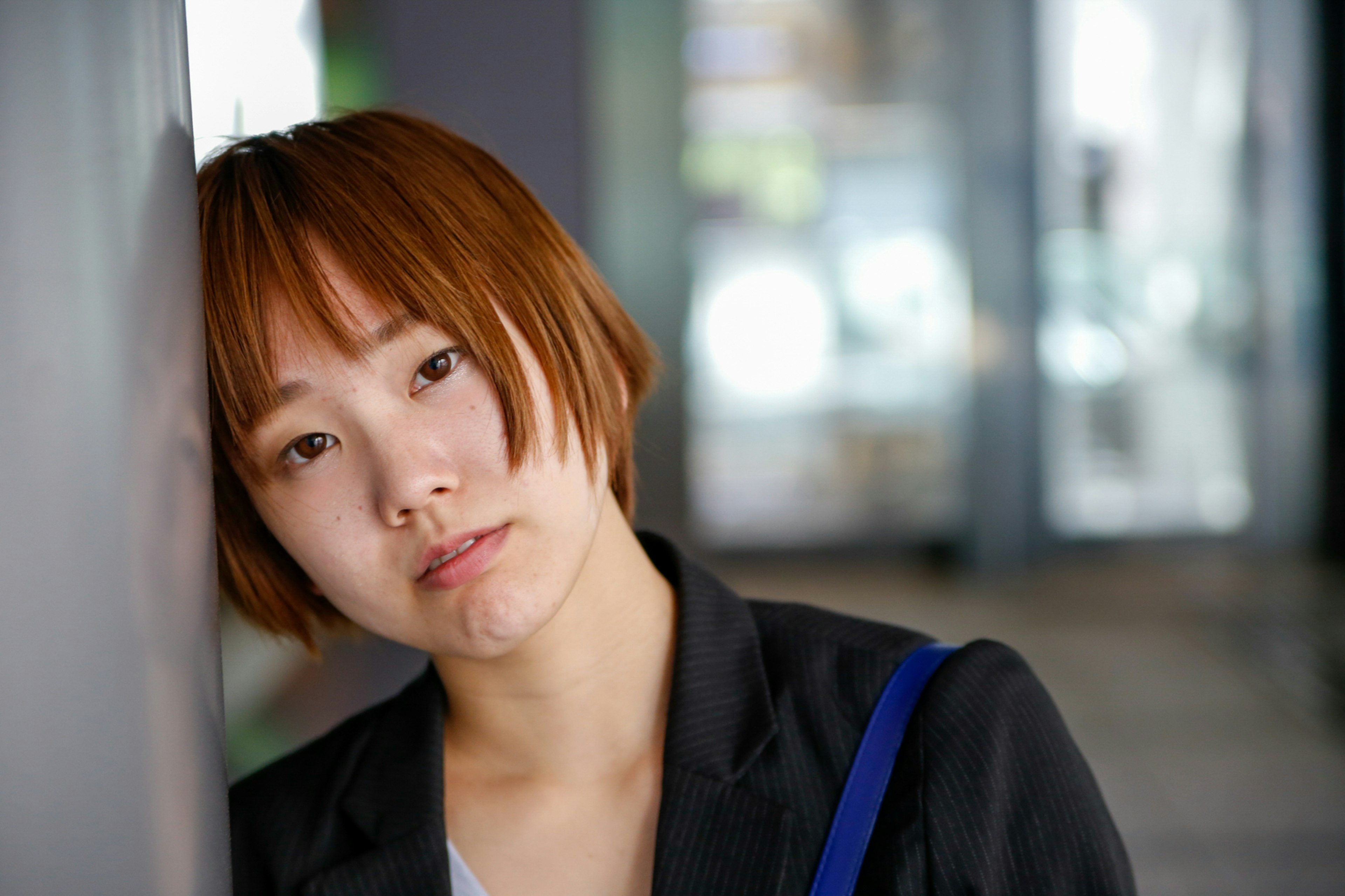 Une femme aux cheveux courts bruns s'appuyant contre un mur avec une expression pensive