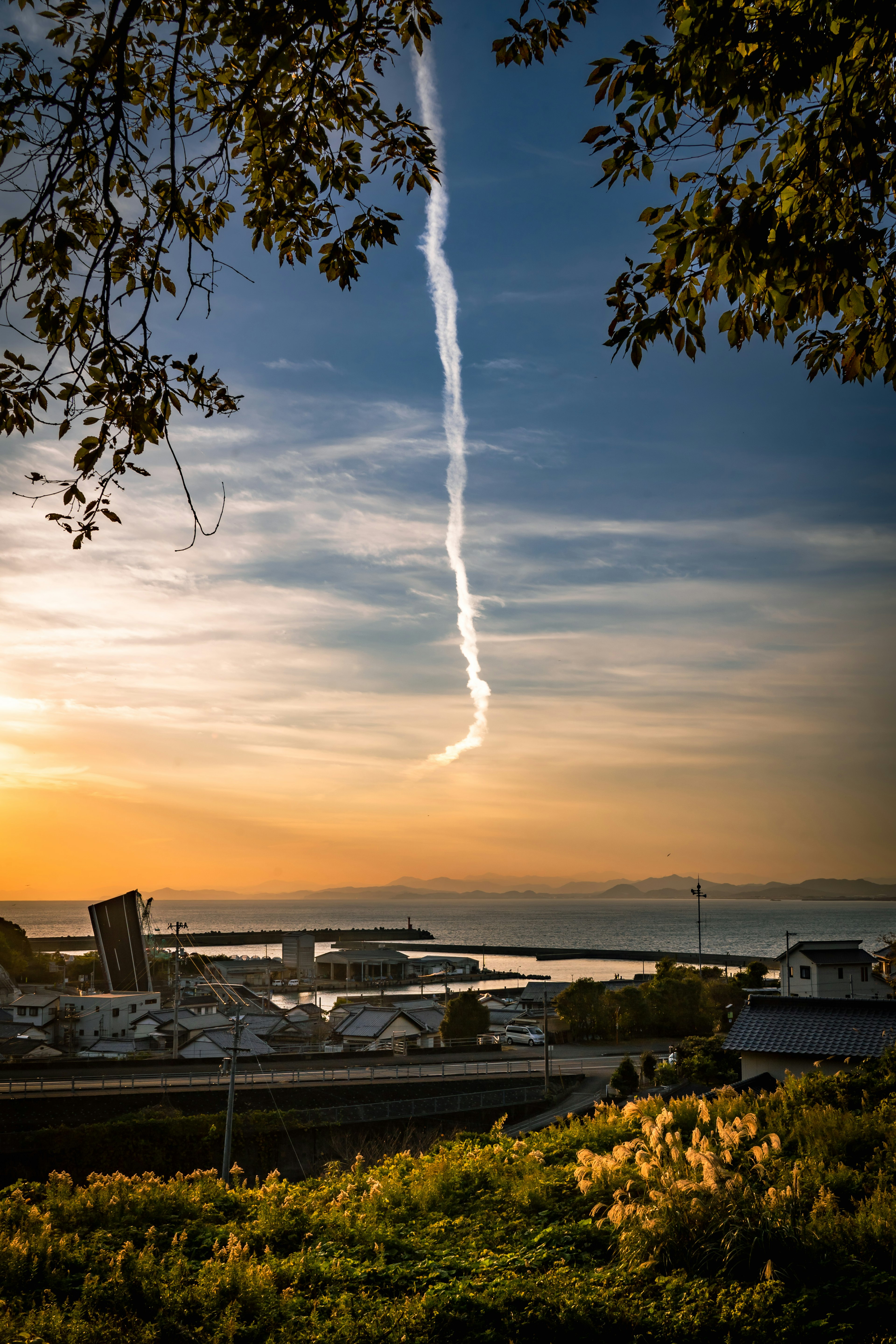 Scenic view of a harbor at sunset with a vapor trail in the sky