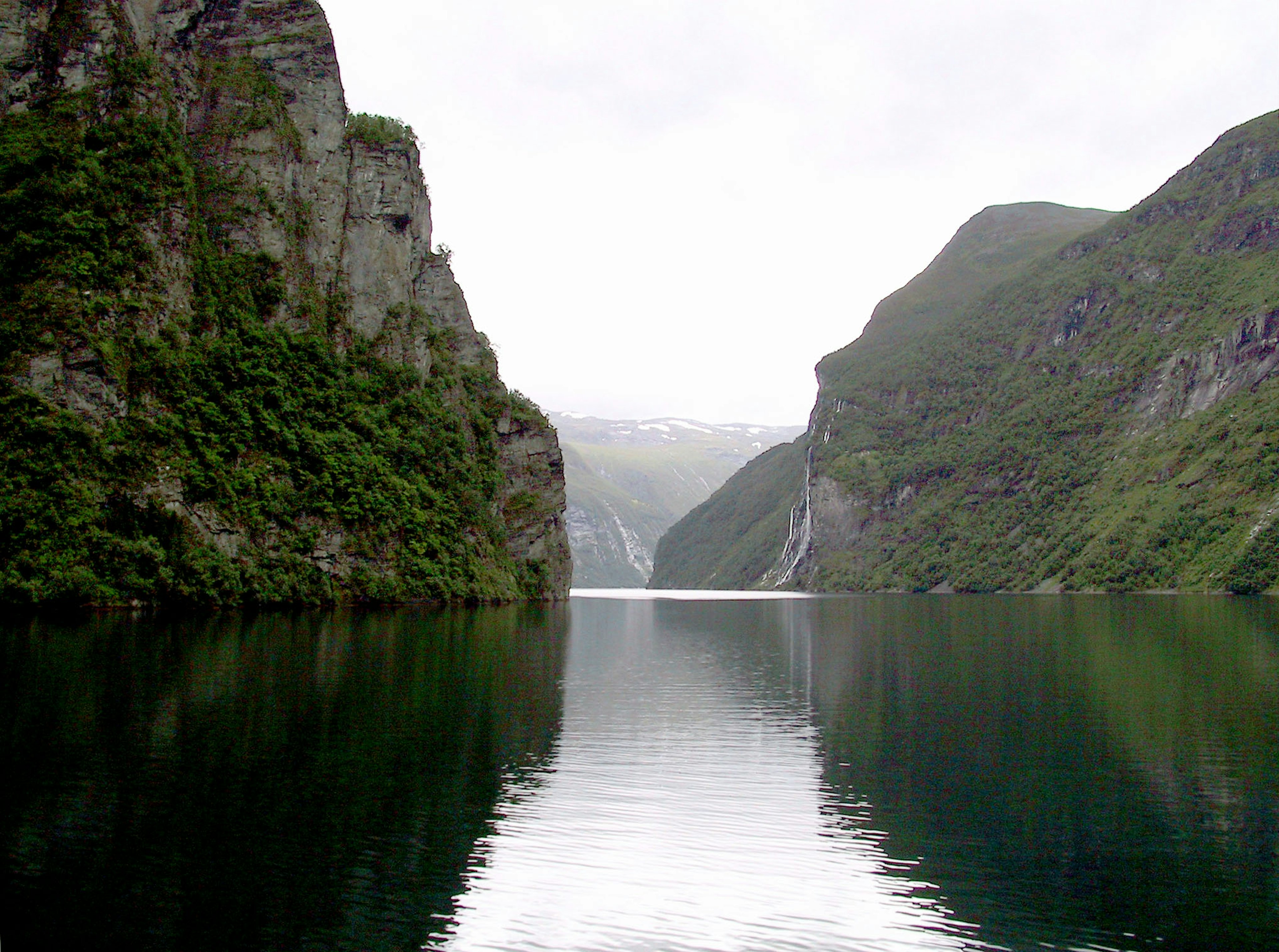 Pemandangan fjord yang tenang dikelilingi oleh gunung hijau