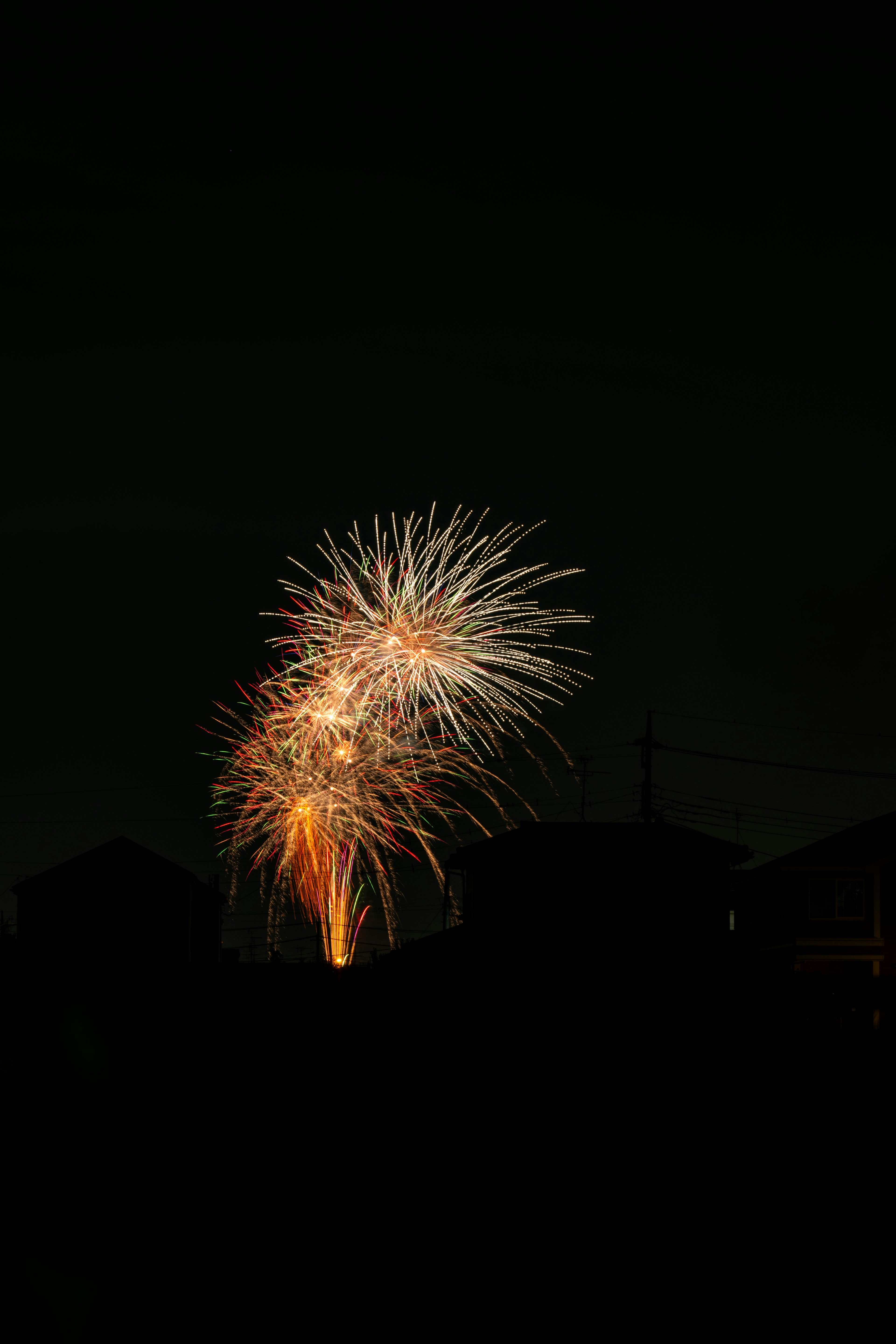 夜空に輝く花火の爆発とシルエットの家々