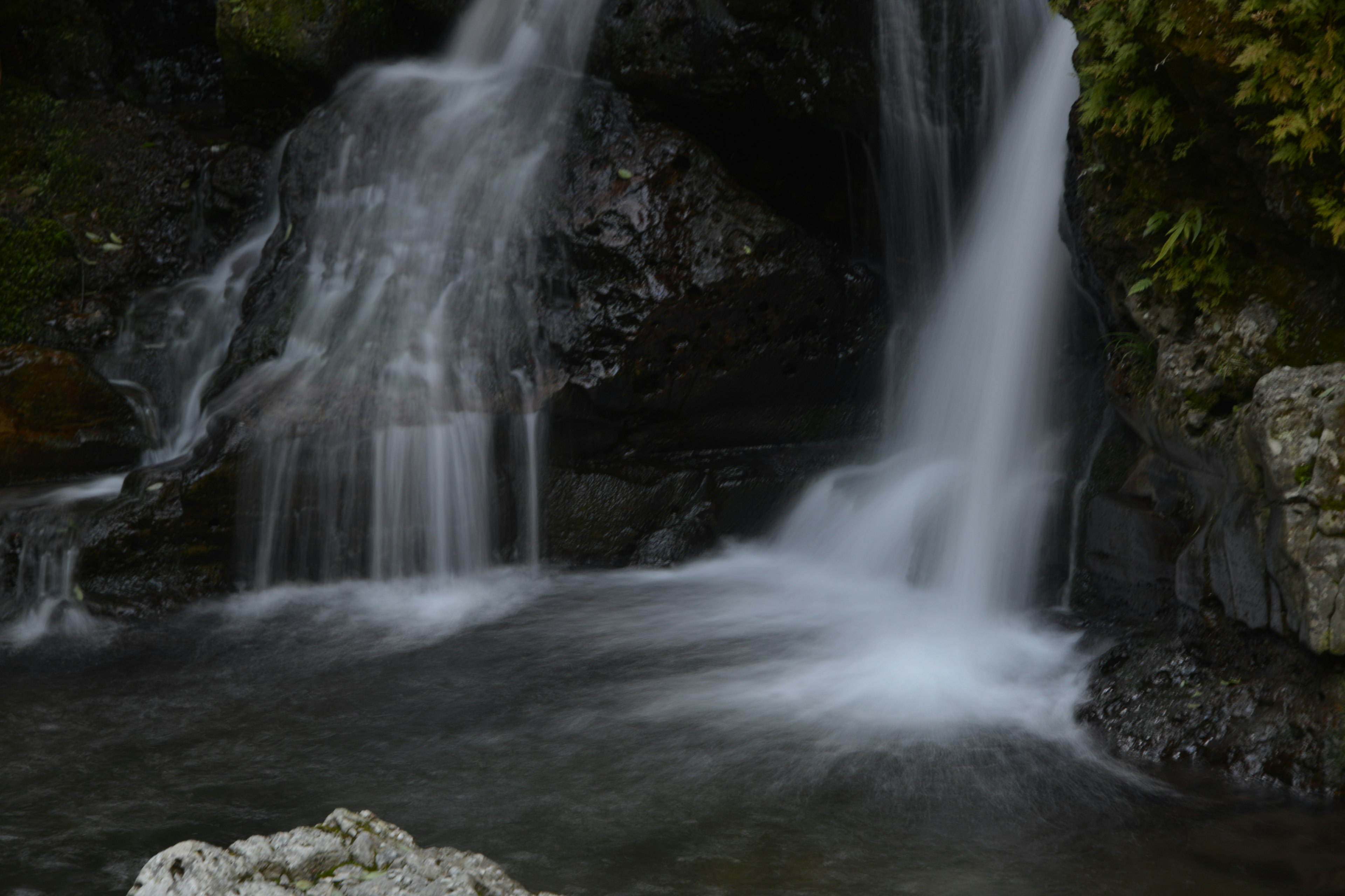 Air terjun tenang yang mengalir ke kolam yang tenang dikelilingi oleh pepohonan hijau