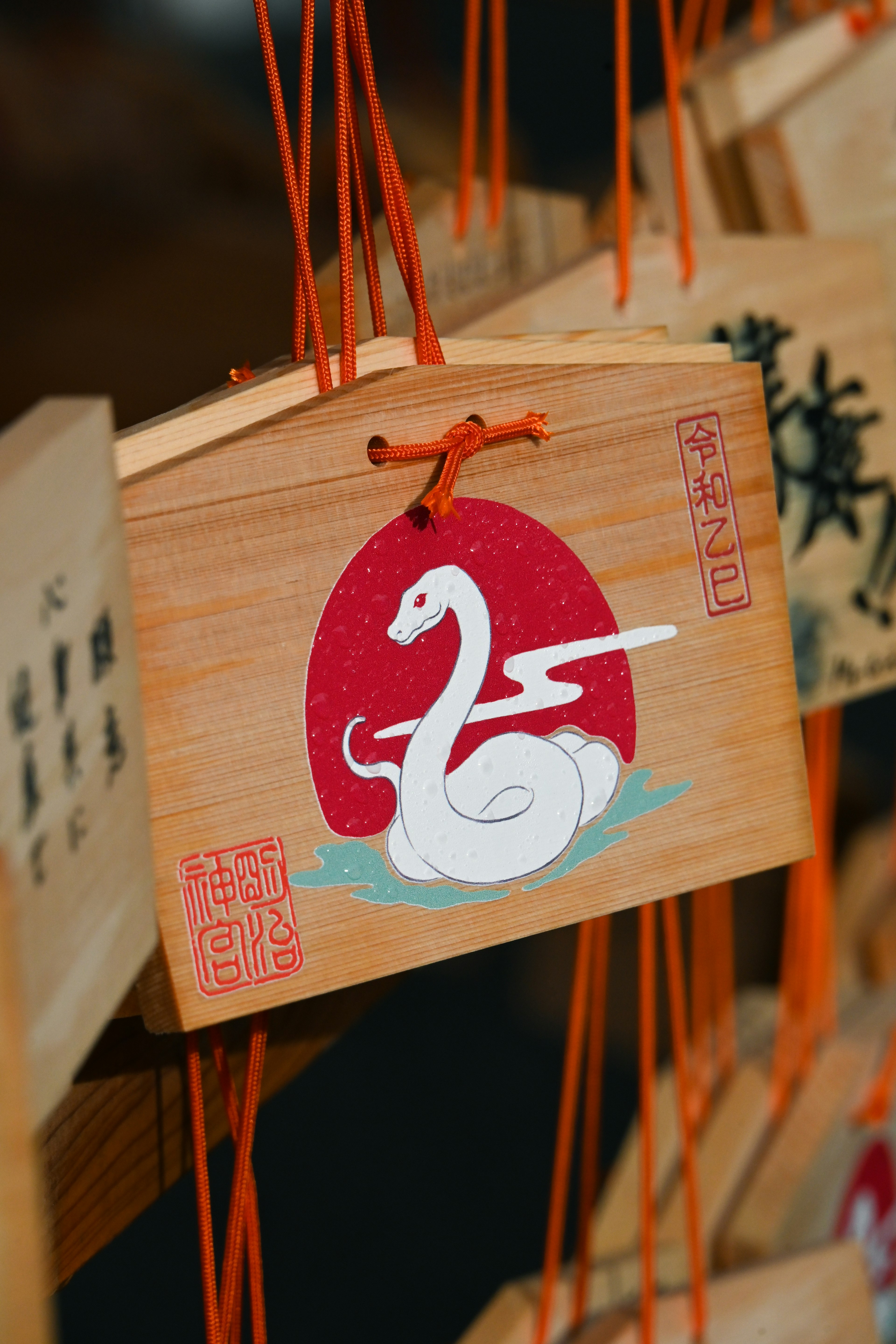 Wooden ema featuring a white snake illustration within a red circle