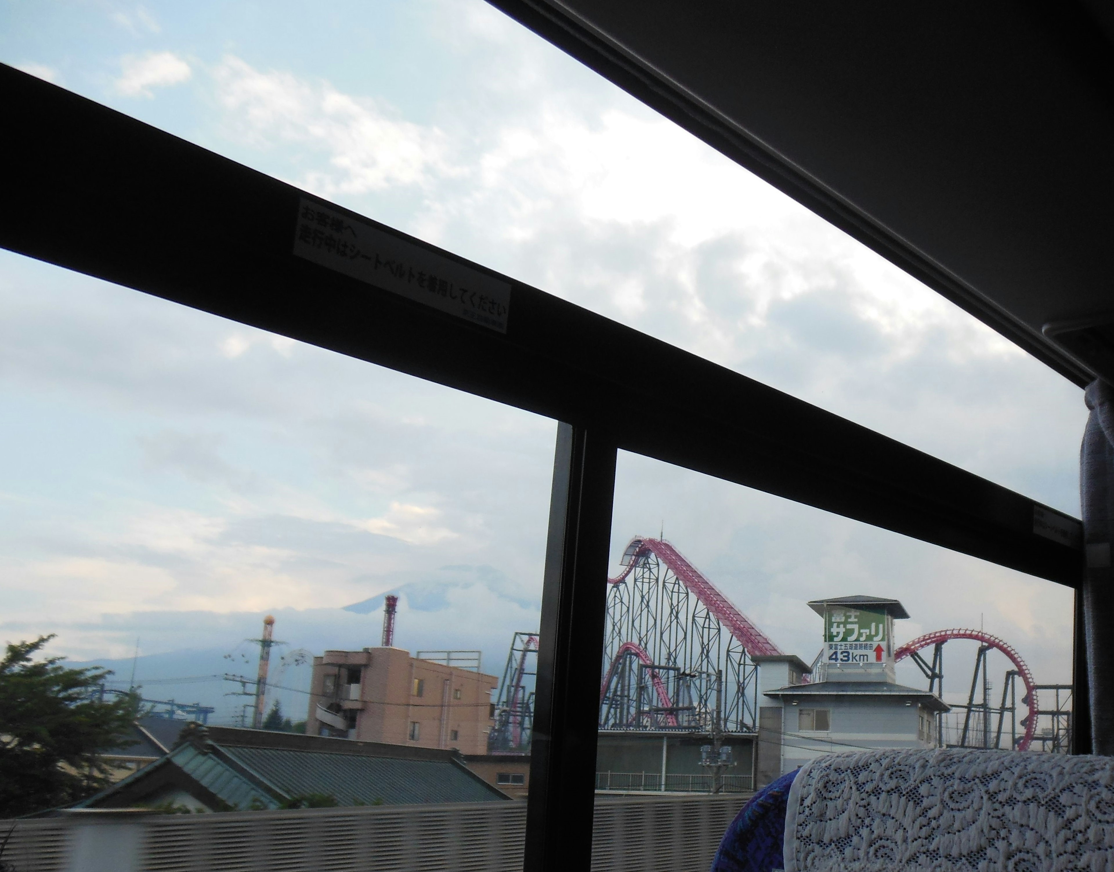 View from a bus window showing an amusement park with a roller coaster and Ferris wheel