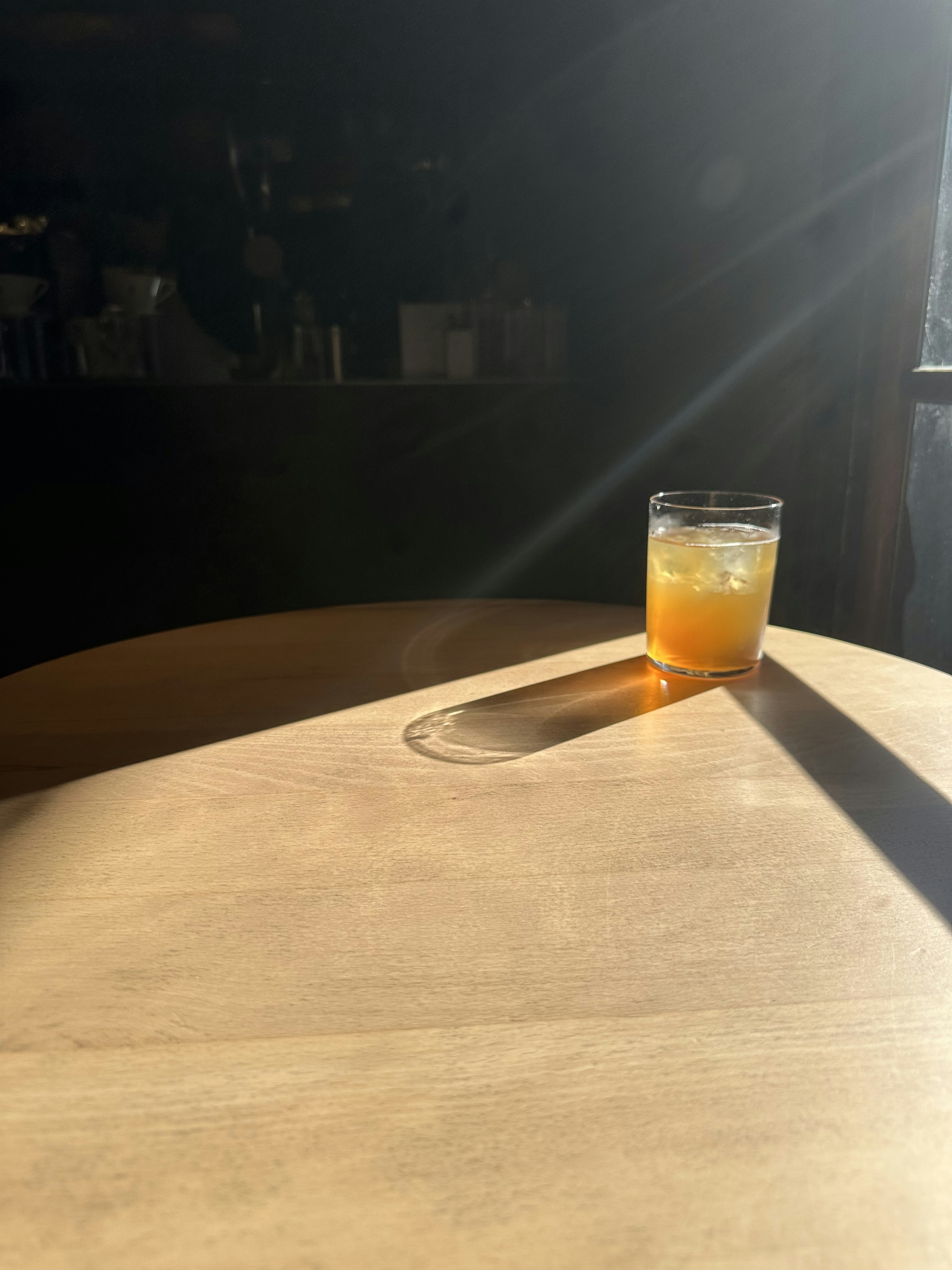 Un vaso de bebida naranja sobre una mesa de madera iluminada por la luz solar