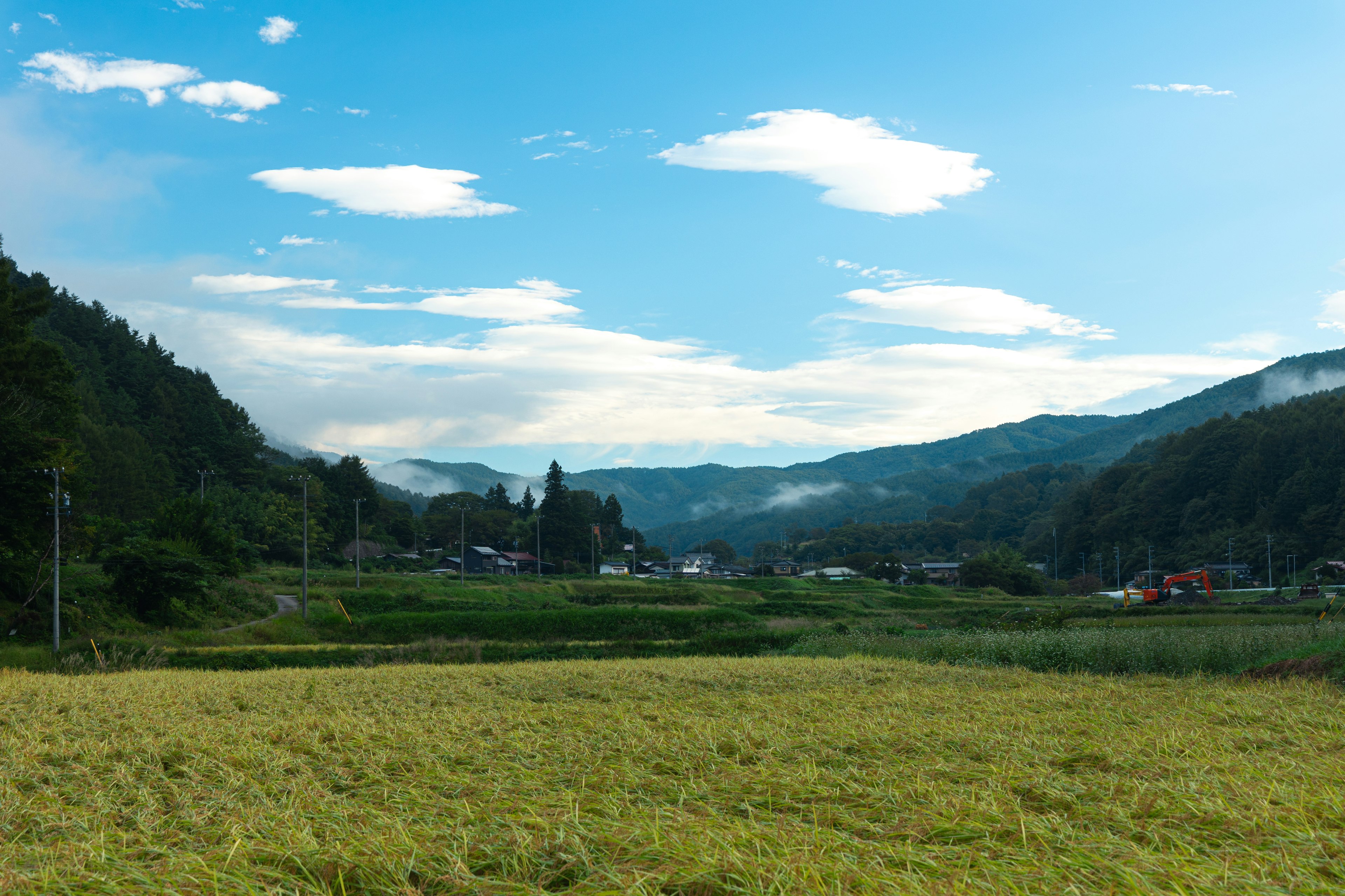 Pemandangan pedesaan yang indah dengan langit biru dan awan putih dikelilingi pegunungan