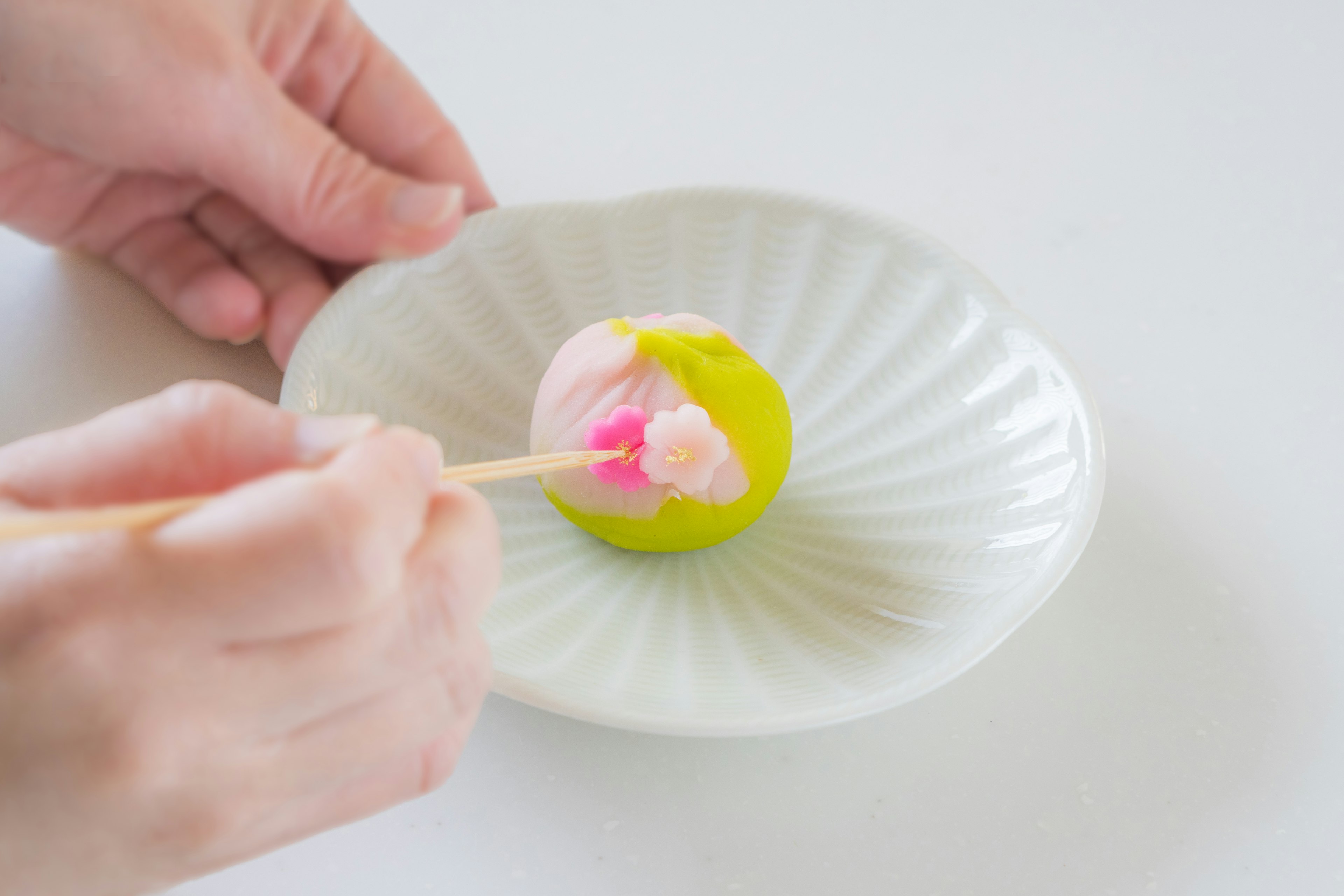 A hand using chopsticks to handle colorful Japanese sweets on a white plate