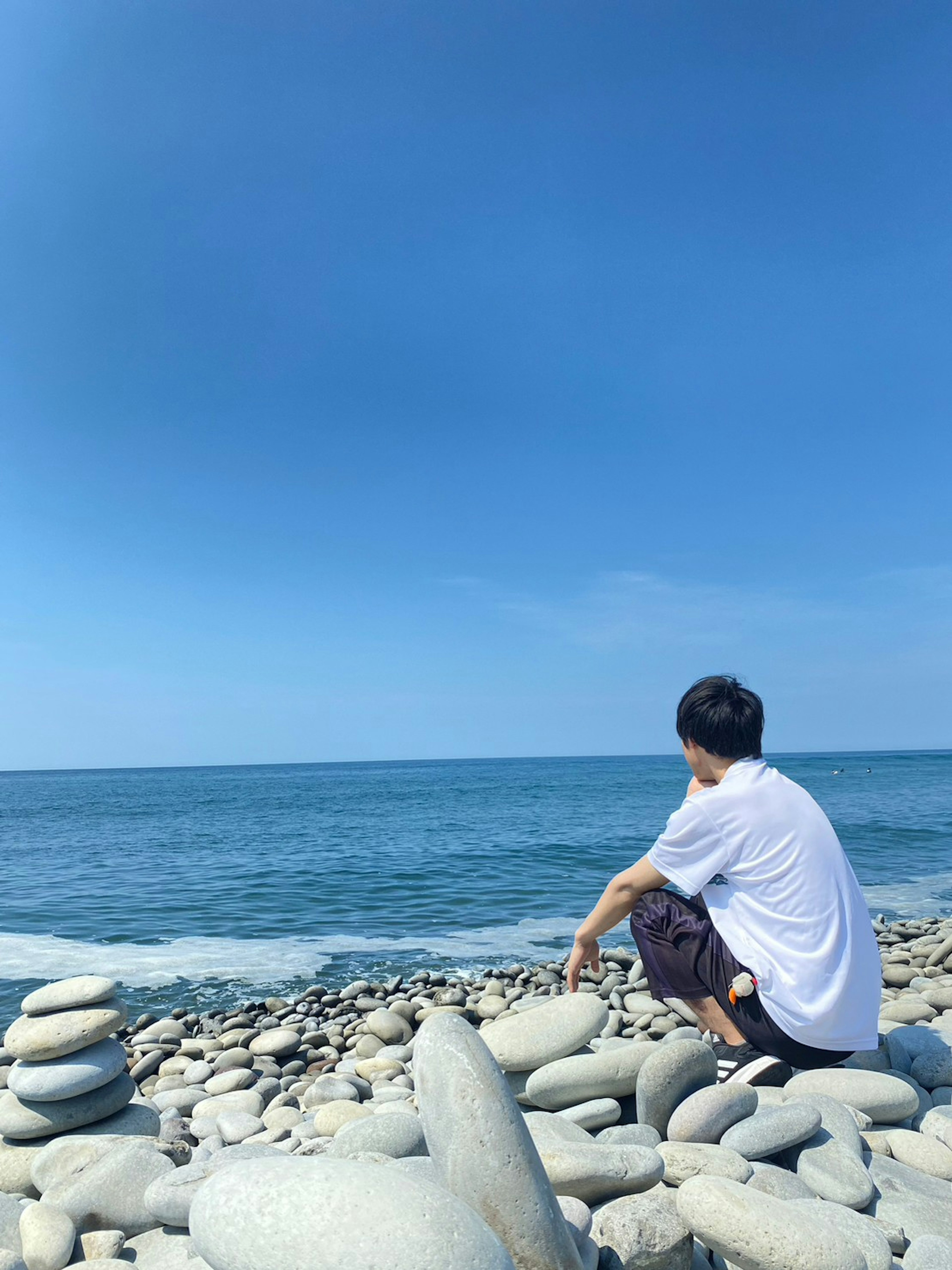 Persona sentada en piedras junto al mar cielo azul claro y océano tranquilo