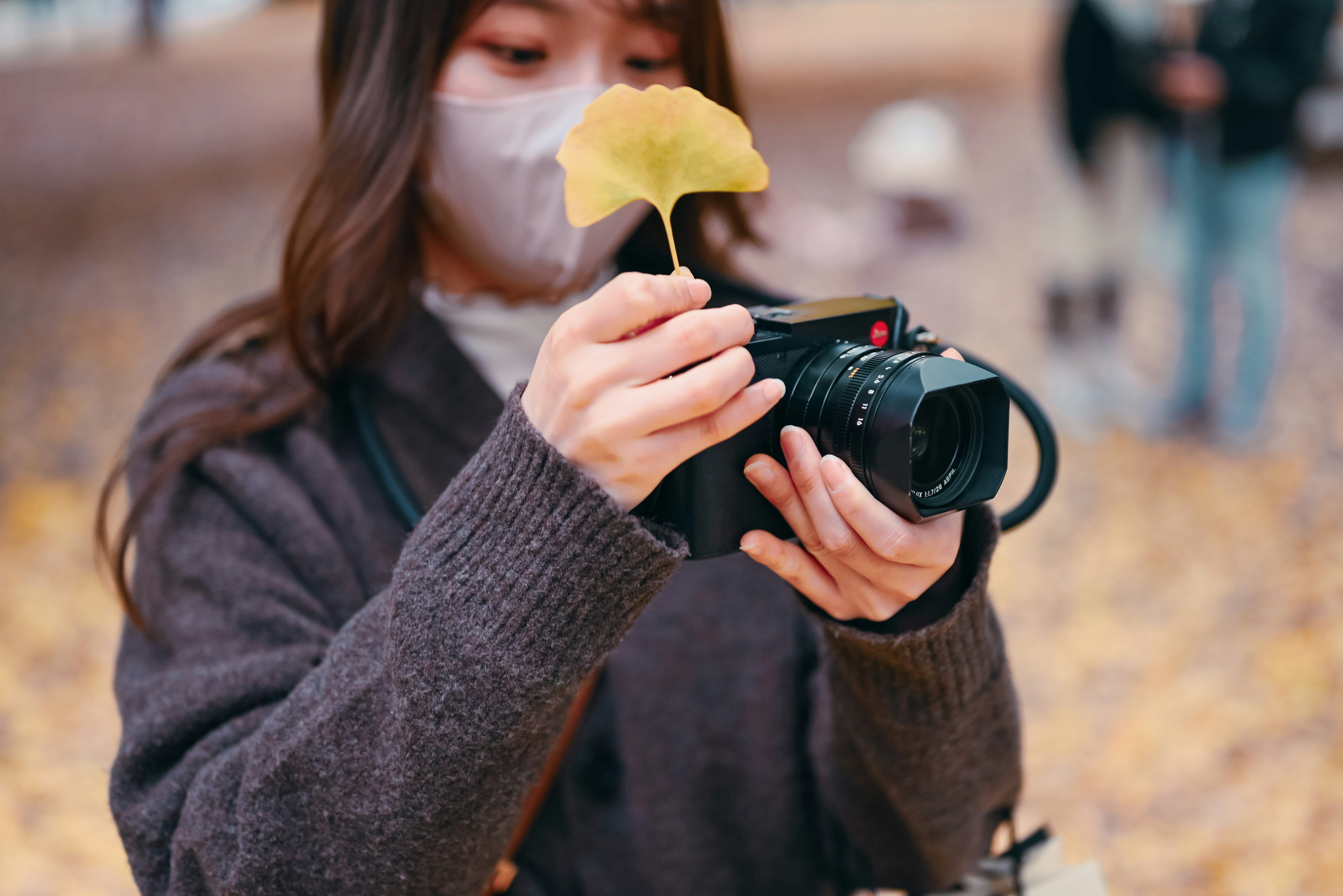 カメラを持っている女性が黄色い葉を手に持っている写真