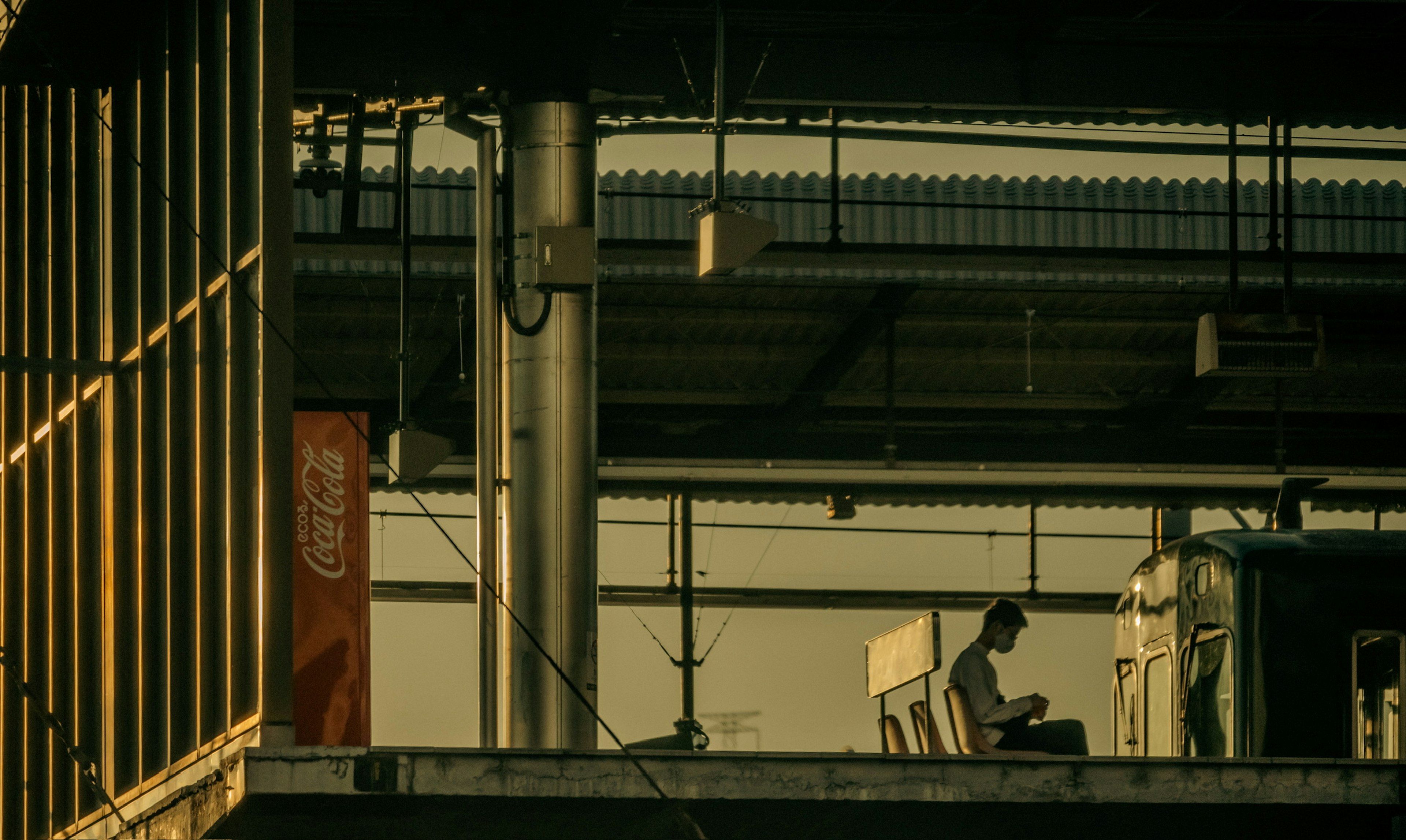 Eine Person sitzt auf einem Bahnsteig mit einem Coca-Cola-Automaten im Hintergrund