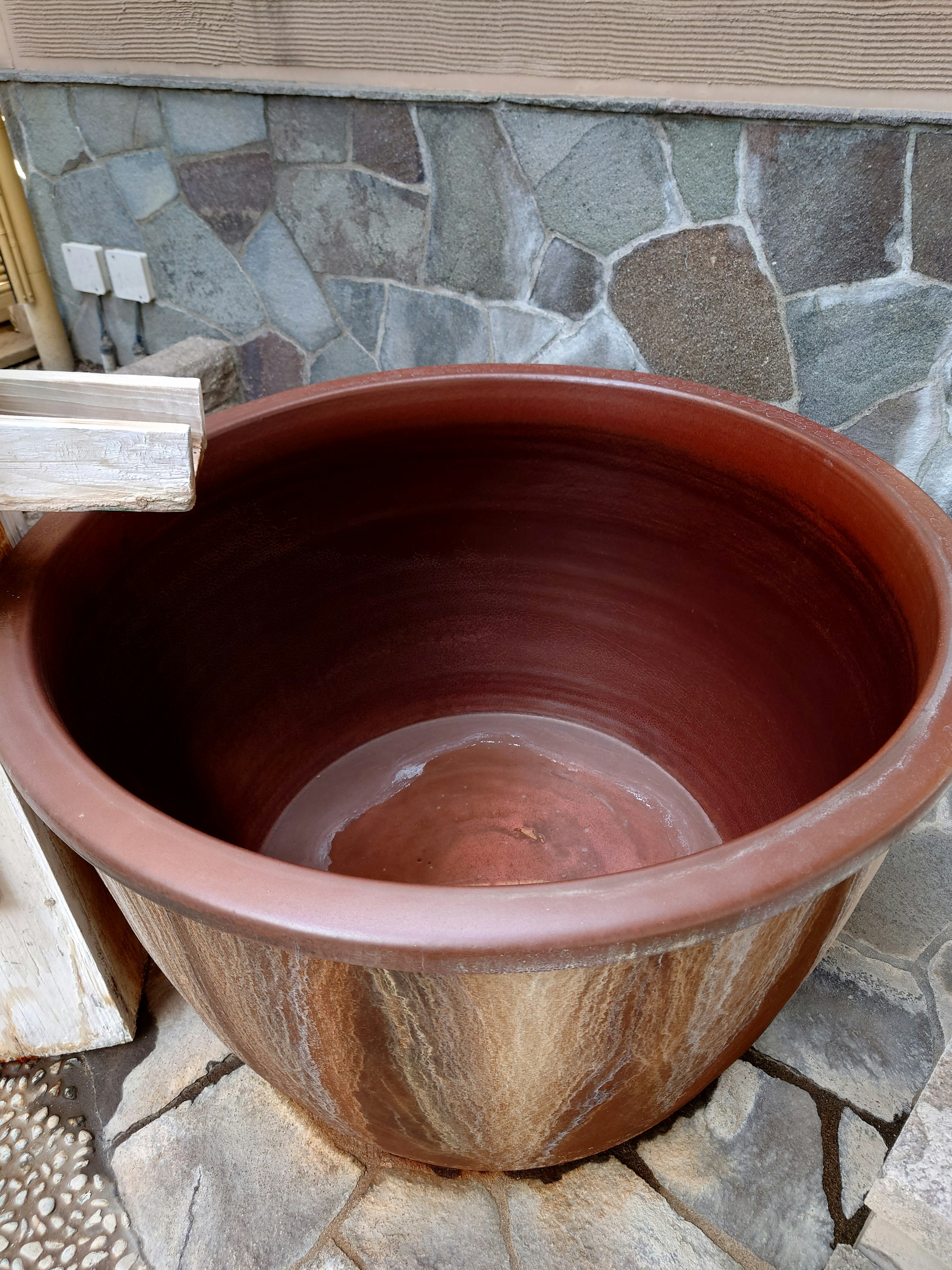 Vaso in ceramica marrone posizionato di fronte a un muro di pietra