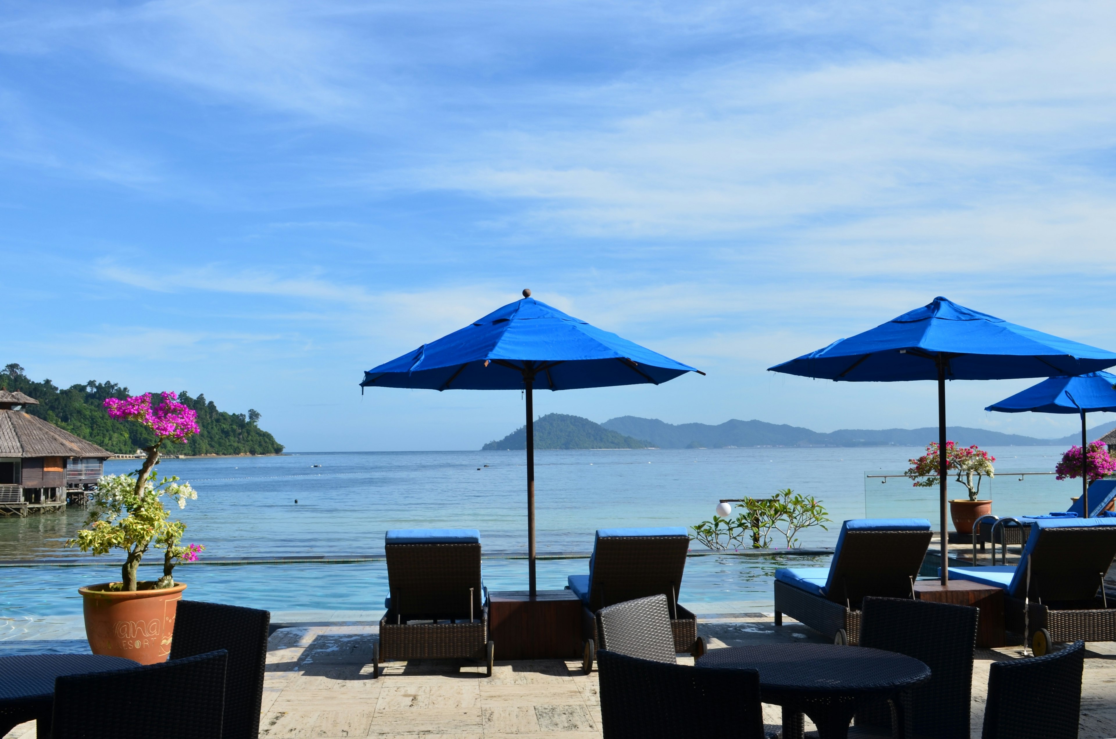 Pemandangan pantai dengan payung biru dan kursi santai, laut tenang, pulau-pulau jauh, langit biru