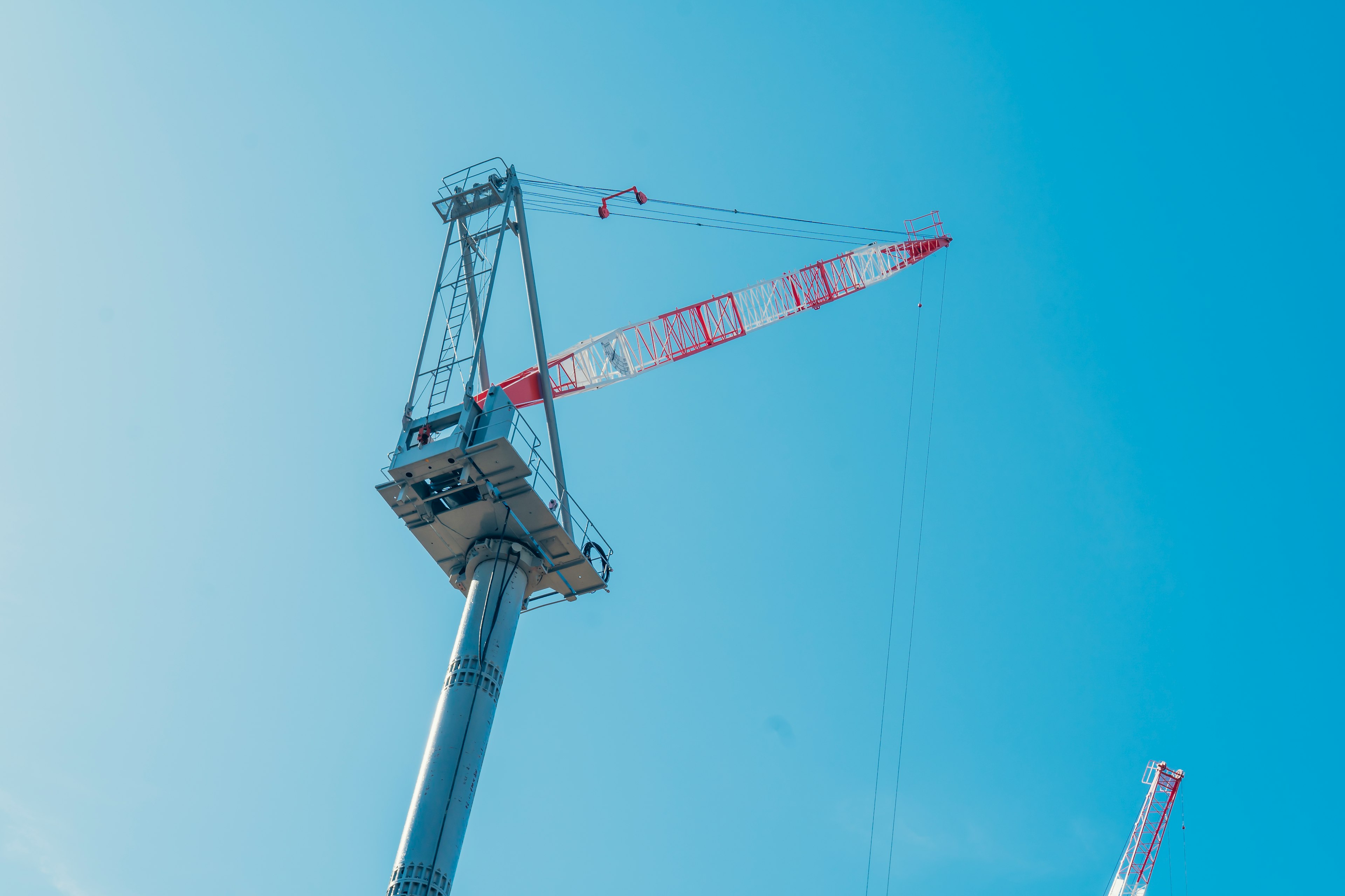 A crane tower under a blue sky with a red and white crane arm