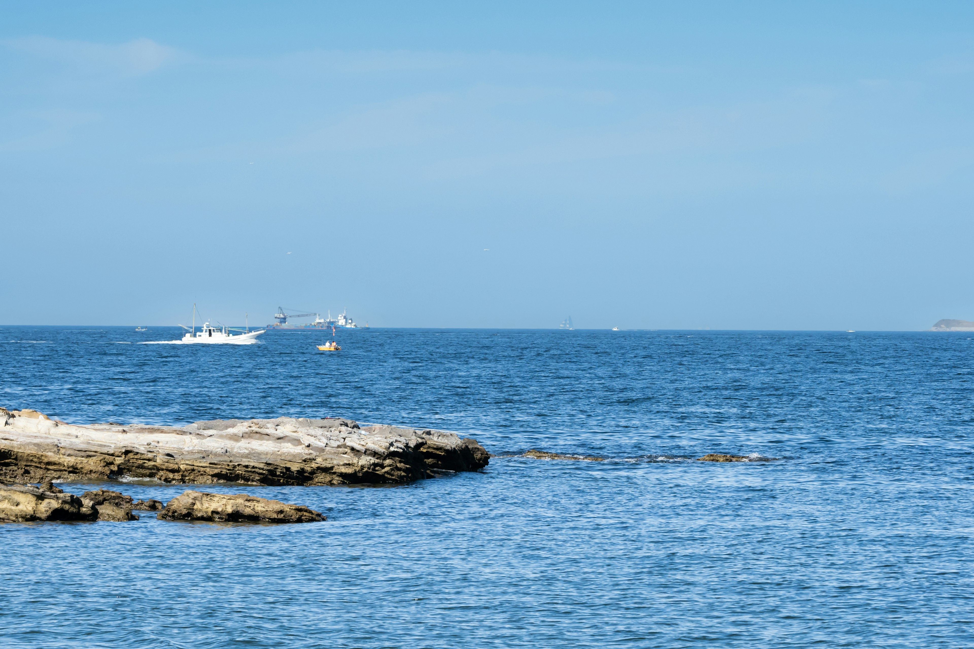 View of blue ocean with rocky shoreline and distant boats