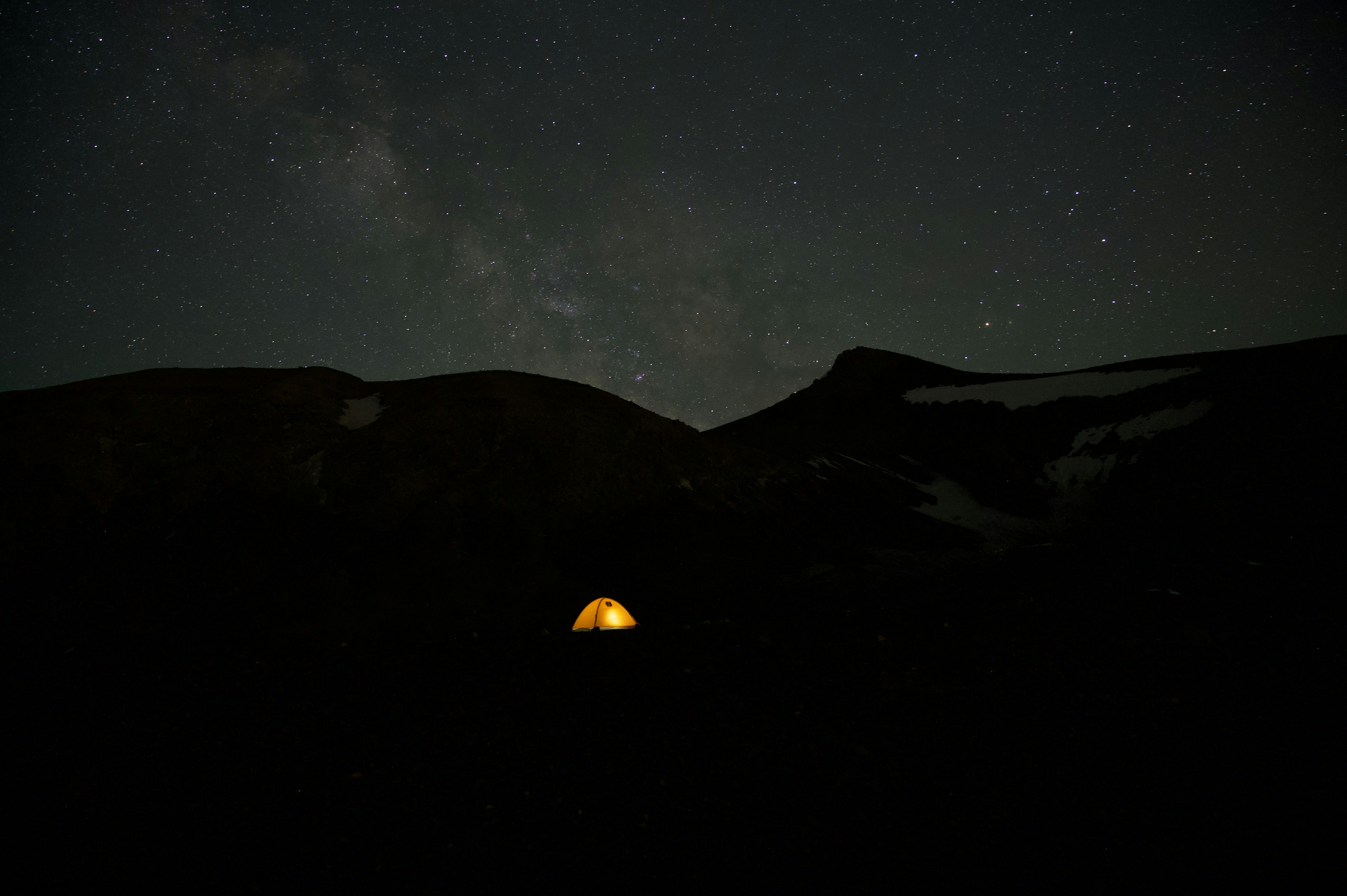 星空の下にある明るいテントと山々のシルエット