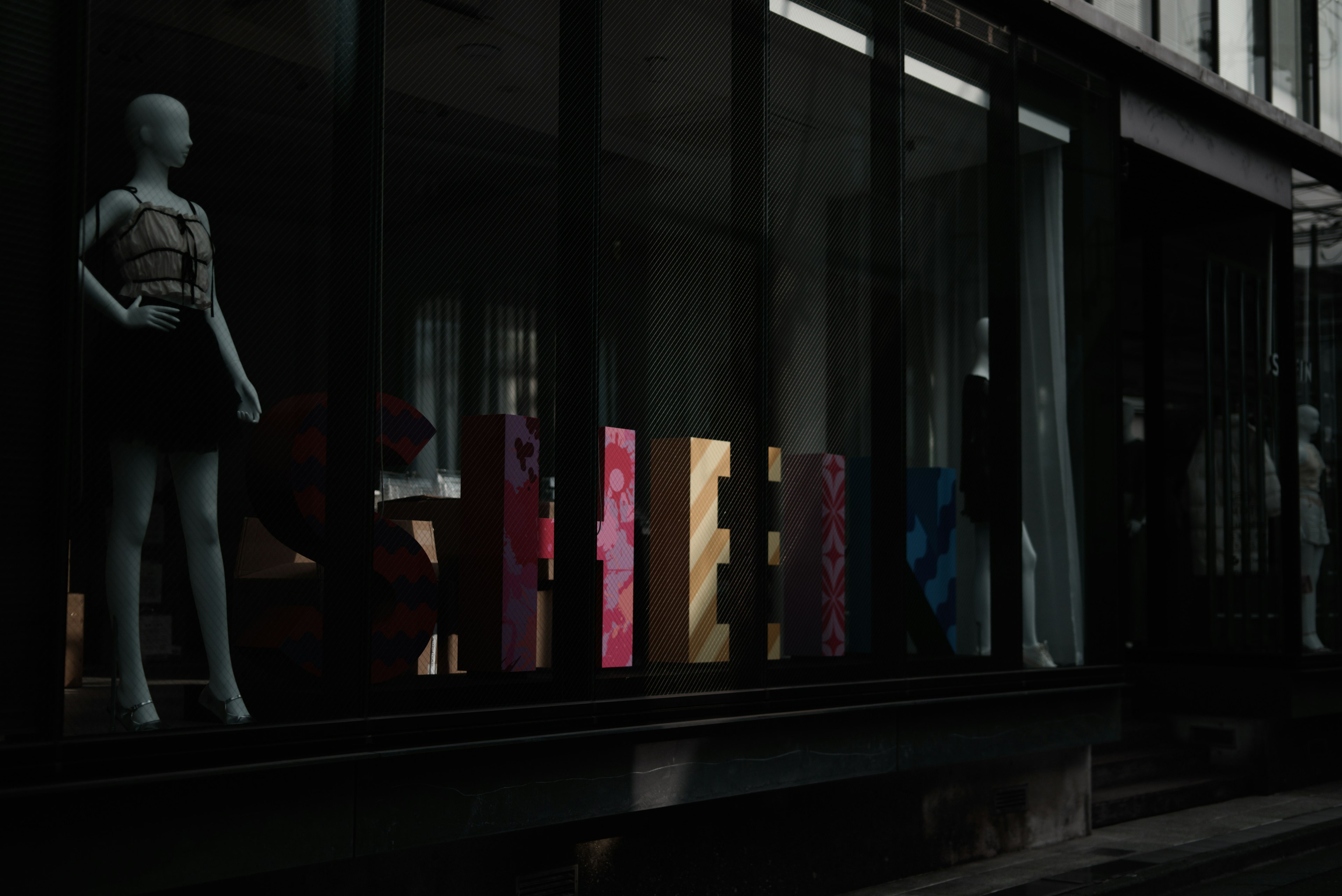 Mannequin dans une vitrine avec des lettres colorées dans une rue sombre