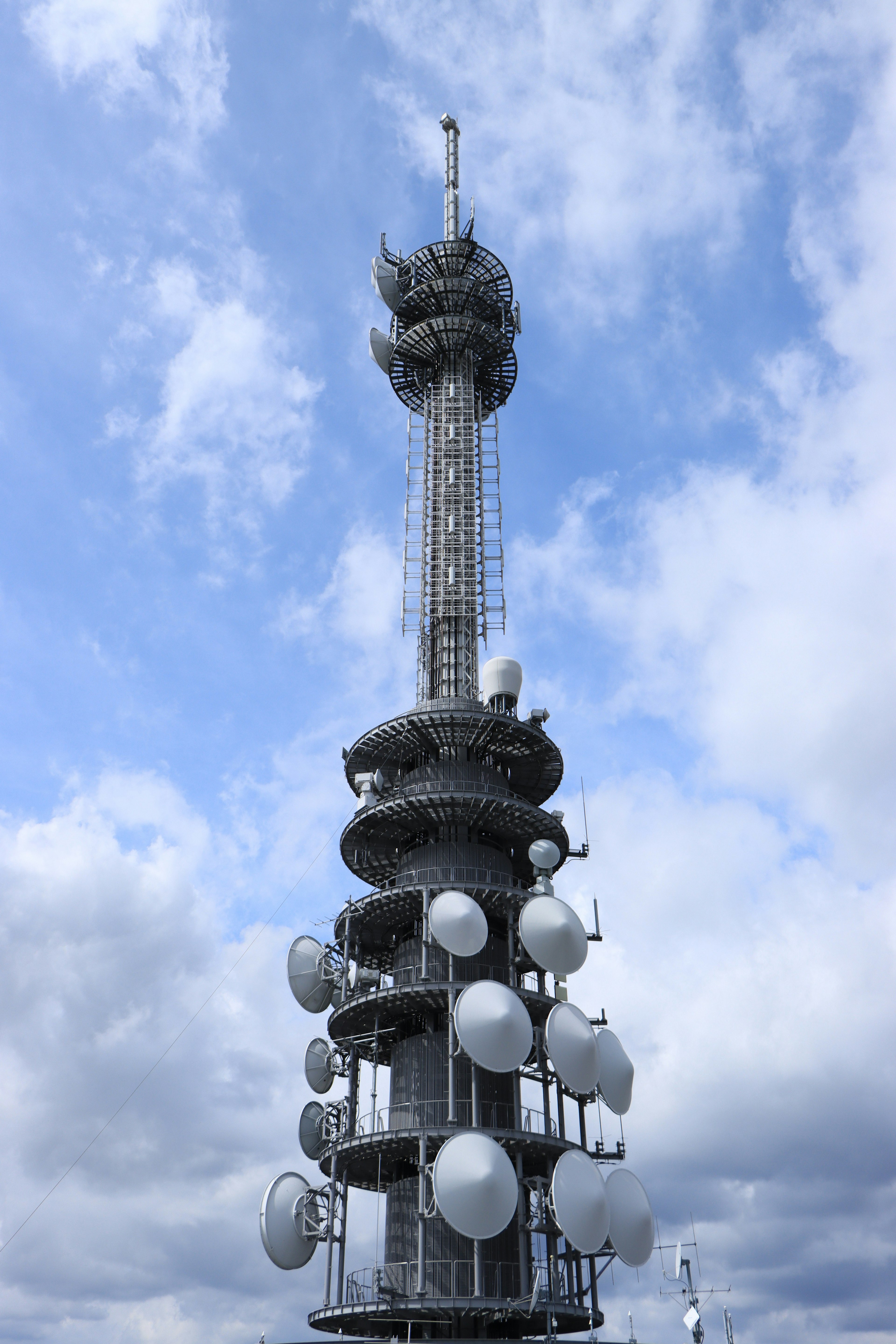 Communication tower with numerous satellite dishes under a blue sky