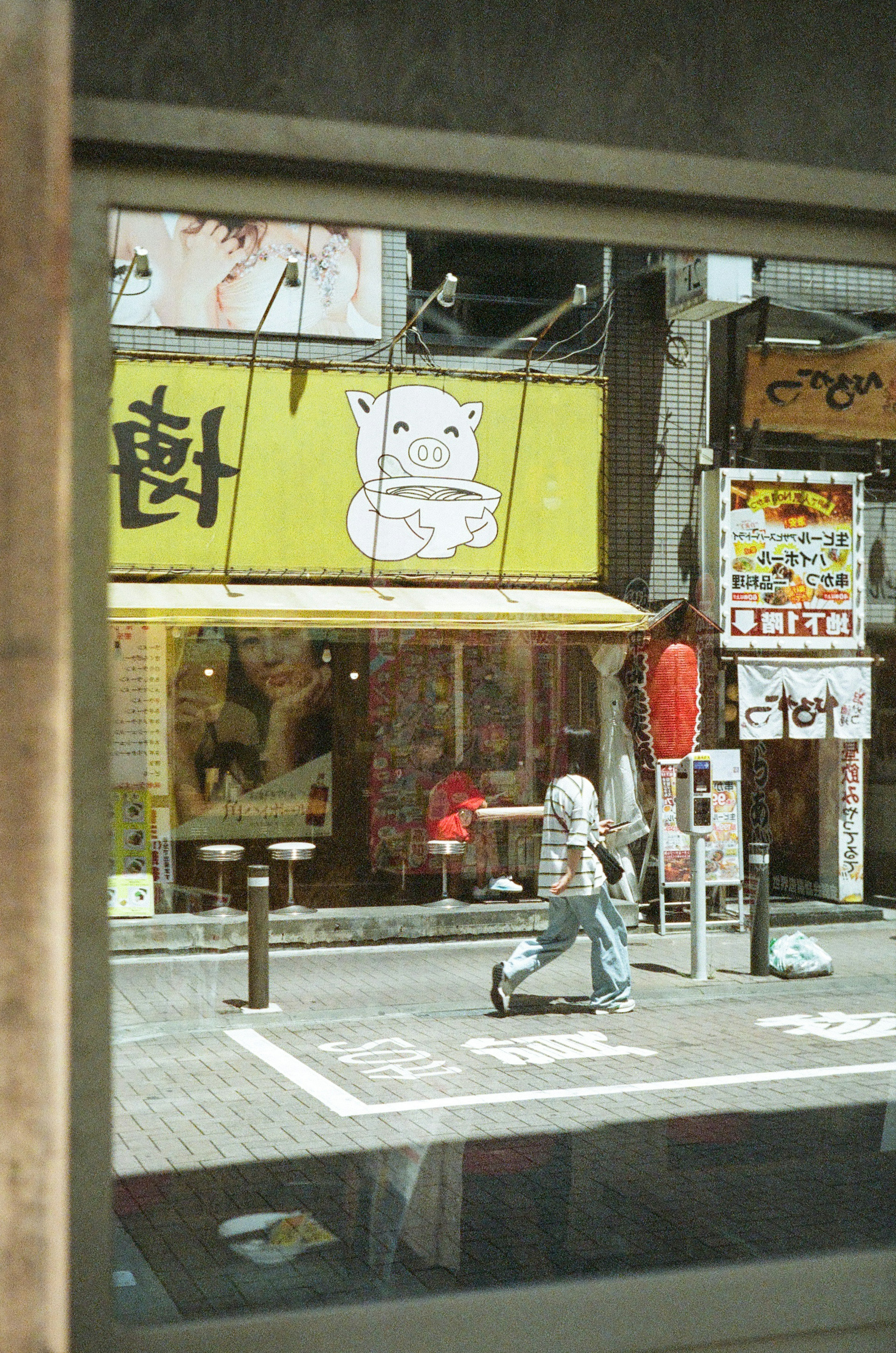 View through a window showing a yellow restaurant sign and a person walking on the street