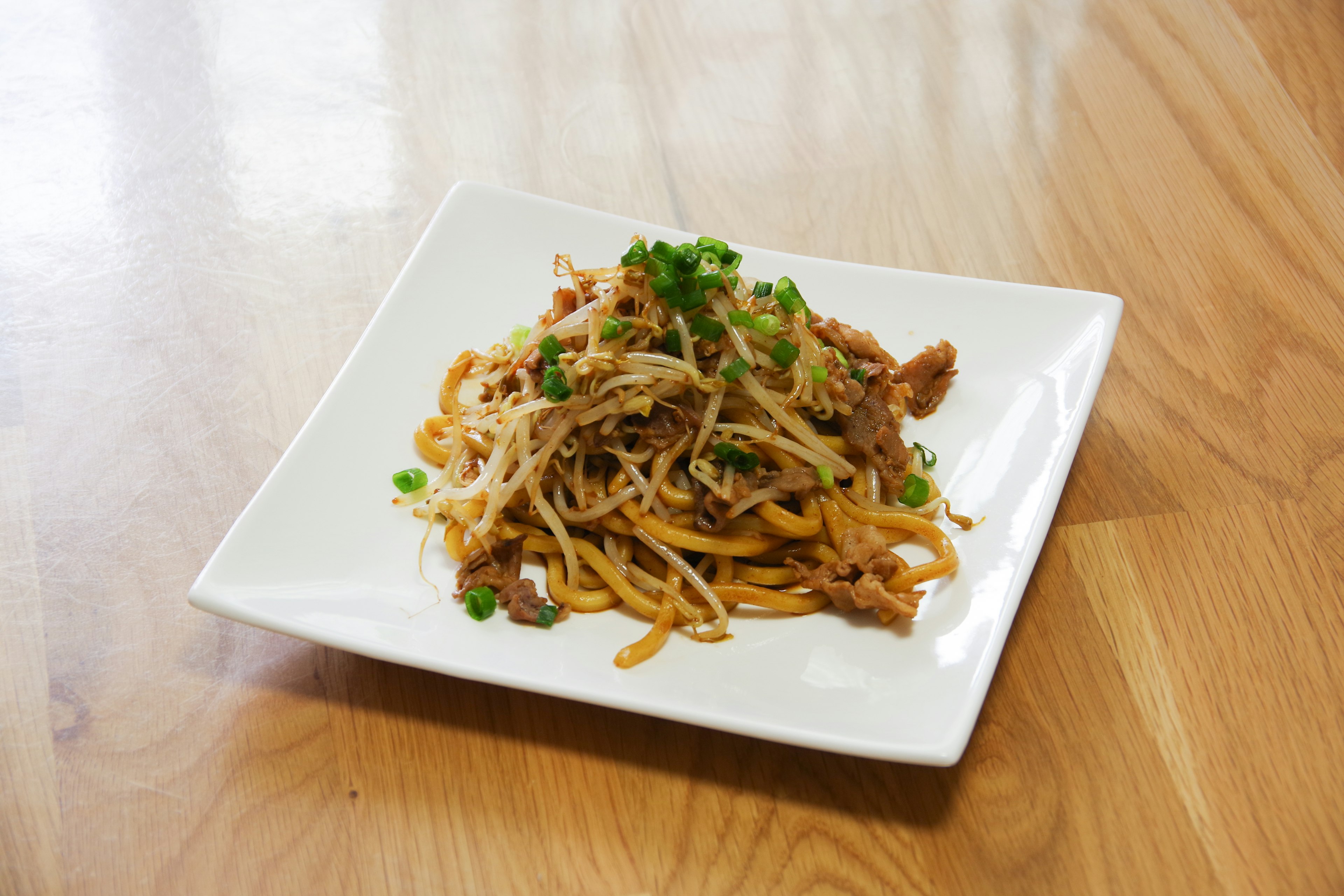 Mie goreng yang dihiasi dengan bawang hijau cincang di atas piring putih